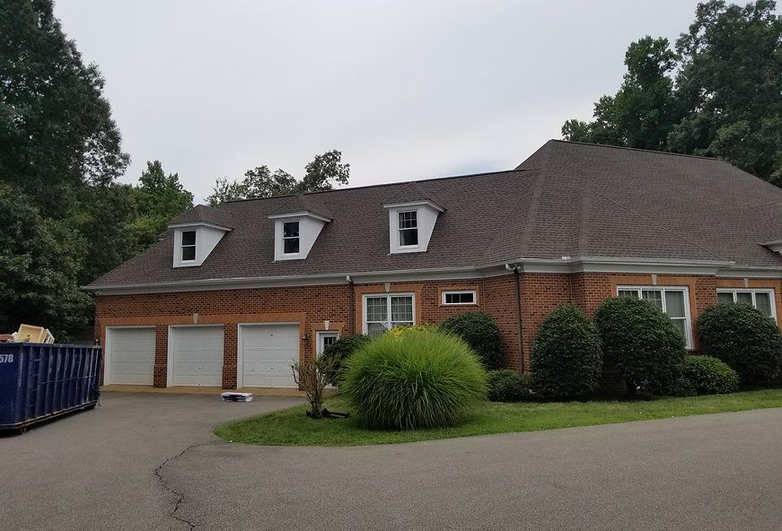 Red brick house with a brown shingled roof, three-car garage, and dormer windows, cloudy sky.