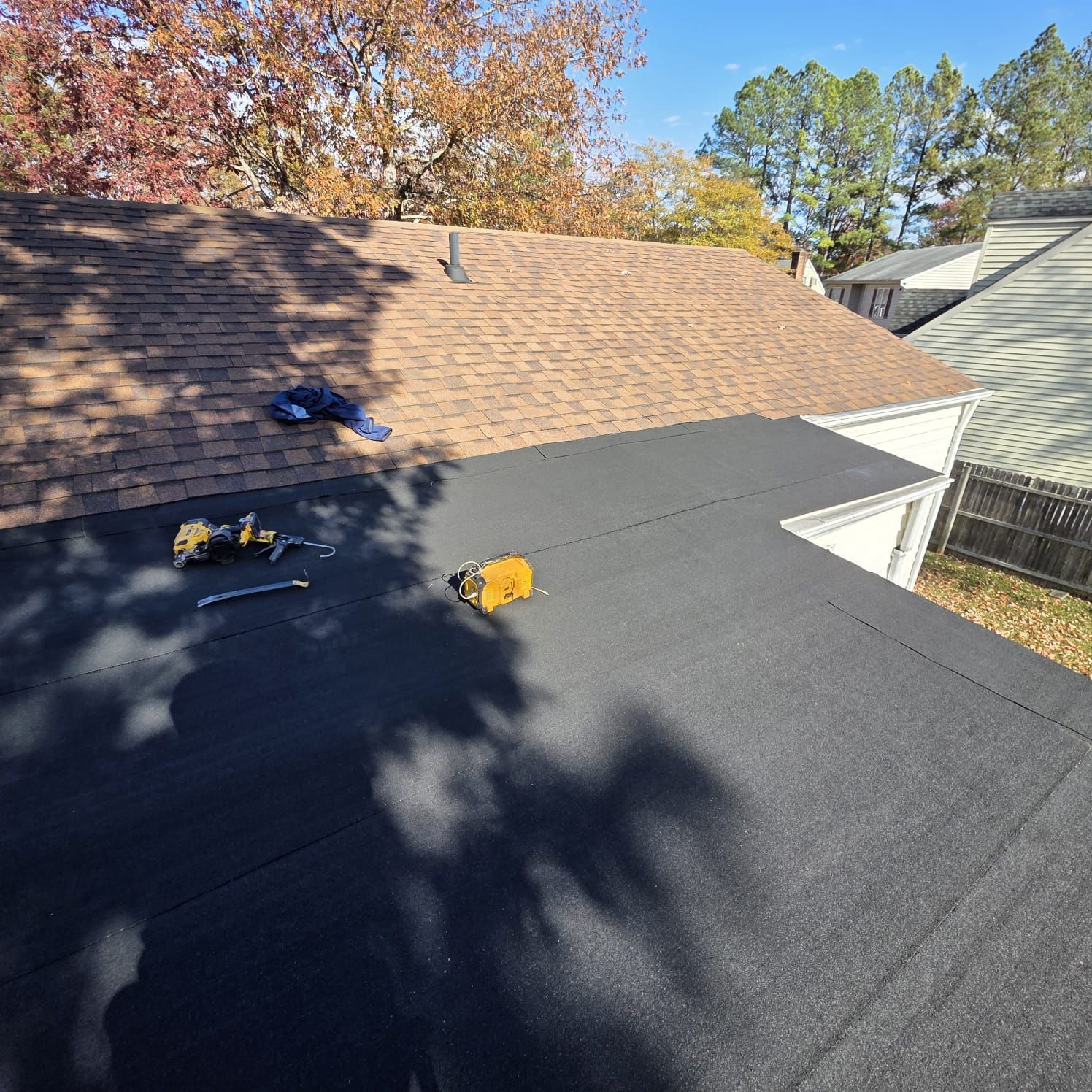 Black flat roof next to brown shingled roof with tools visible. Sunny day.