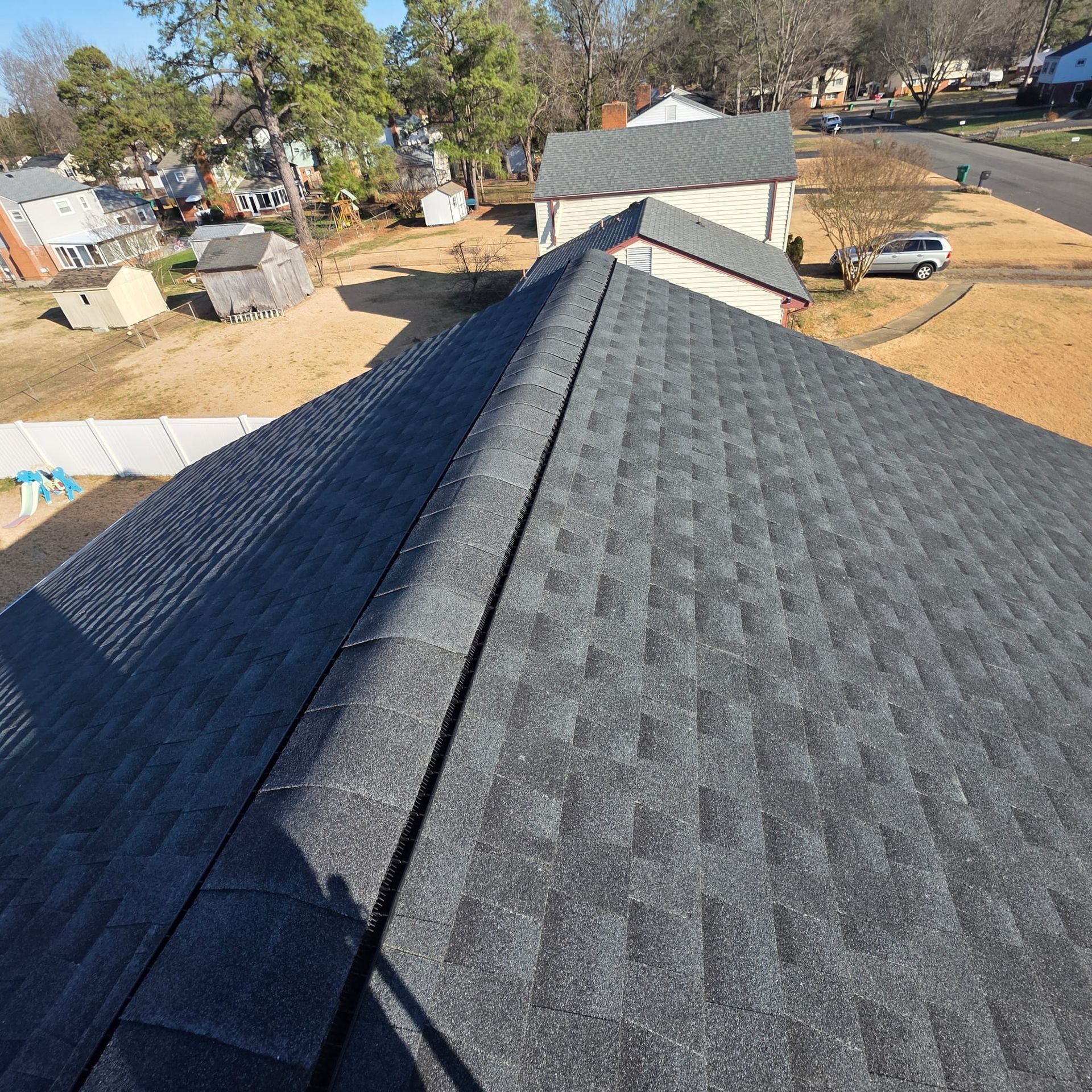 Newly shingled, dark gray roof. Houses, trees, and a road are visible in the background.
