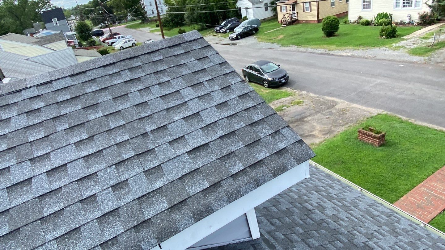 Gray asphalt shingle roof, aerial view overlooking a residential street and lawns.