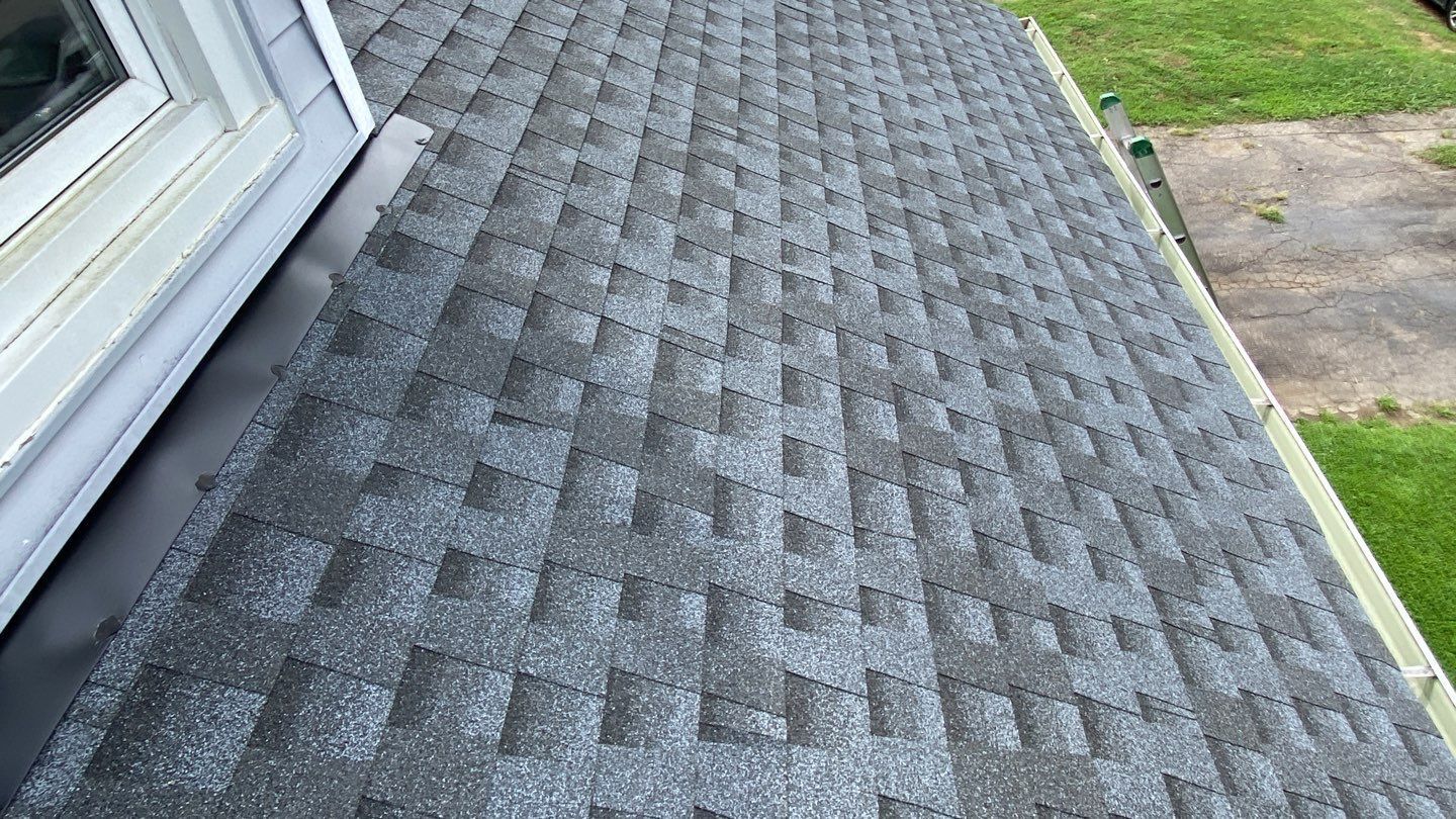 Close-up view of a dark gray shingled roof with a black metal flashing along the edge, next to a window.