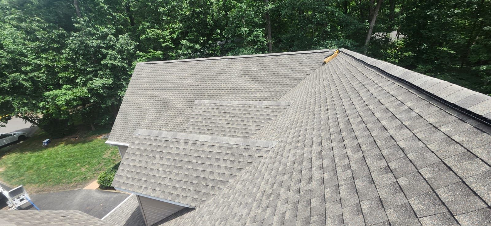Overhead view of a gray asphalt shingle roof surrounded by green trees.