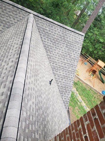 Gray shingled roof with a dark ridge, overlooking a brick wall and a playground.
