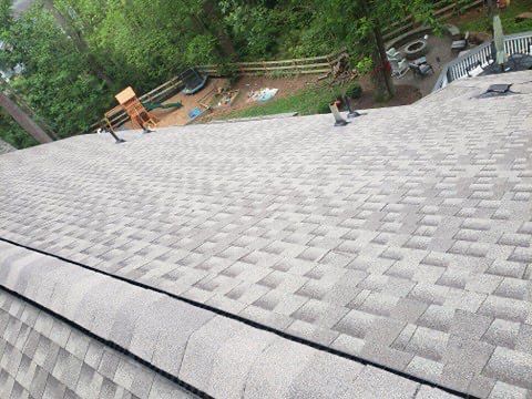 Gray shingle roof, angled view. A person standing on the roof, trees in the background.