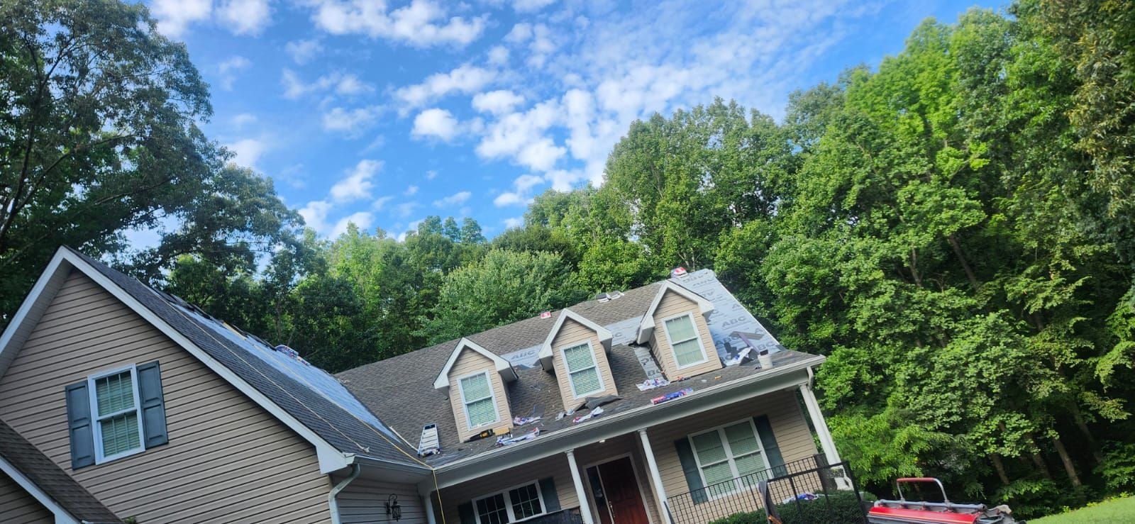 House with solar panels on roof, blue sky with clouds, trees surrounding.