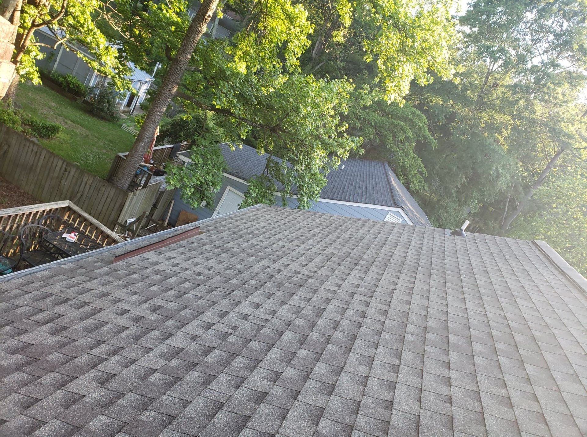 Gray asphalt shingle roof on a house, with trees and a fence in the background.