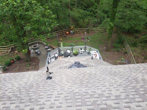 Overhead view of a roof, a deck, and backyard with trees.