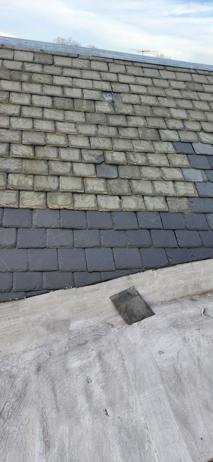 A roof with gray and dark gray slates. A new row of slates is installed at the bottom.