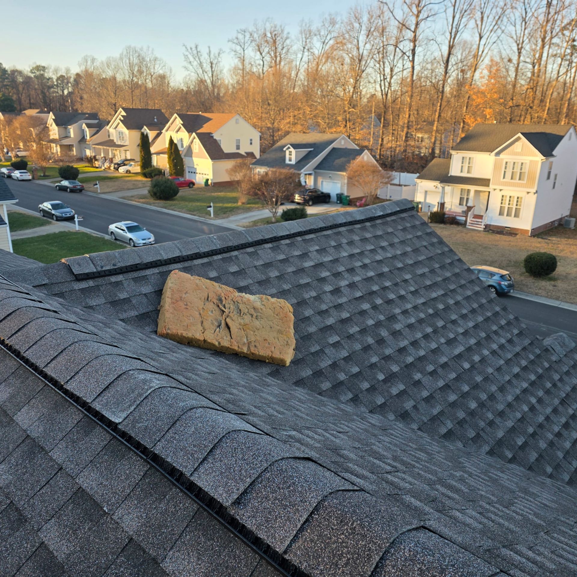 A gray shingled roof with a rectangular foam block on top, overlooking a suburban street with houses and cars.