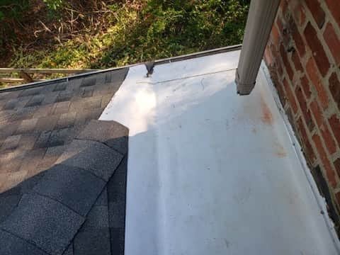Roof with asphalt shingles and metal flashing next to a brick wall and a gutter.