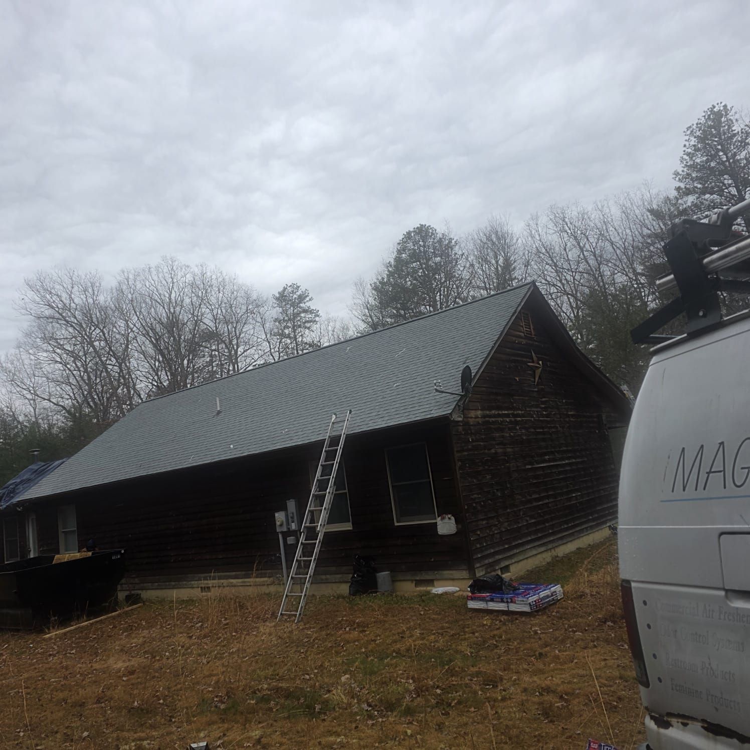 A wooden building with a gray metal roof under a cloudy sky. A ladder leans against the roof.