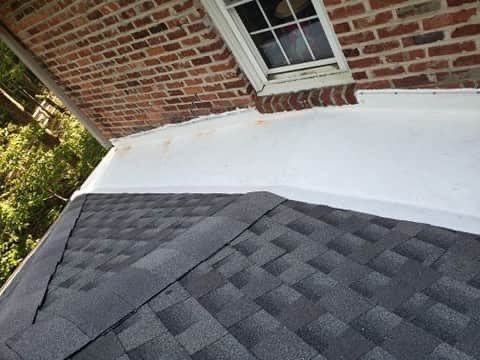 Black asphalt shingle roof meets white flat roof against brick wall with window.