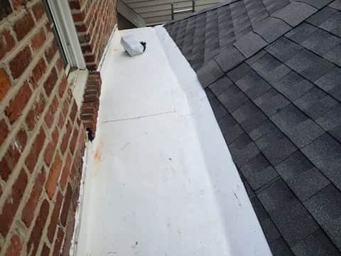 Brick wall next to white painted structure and a dark shingle roof.