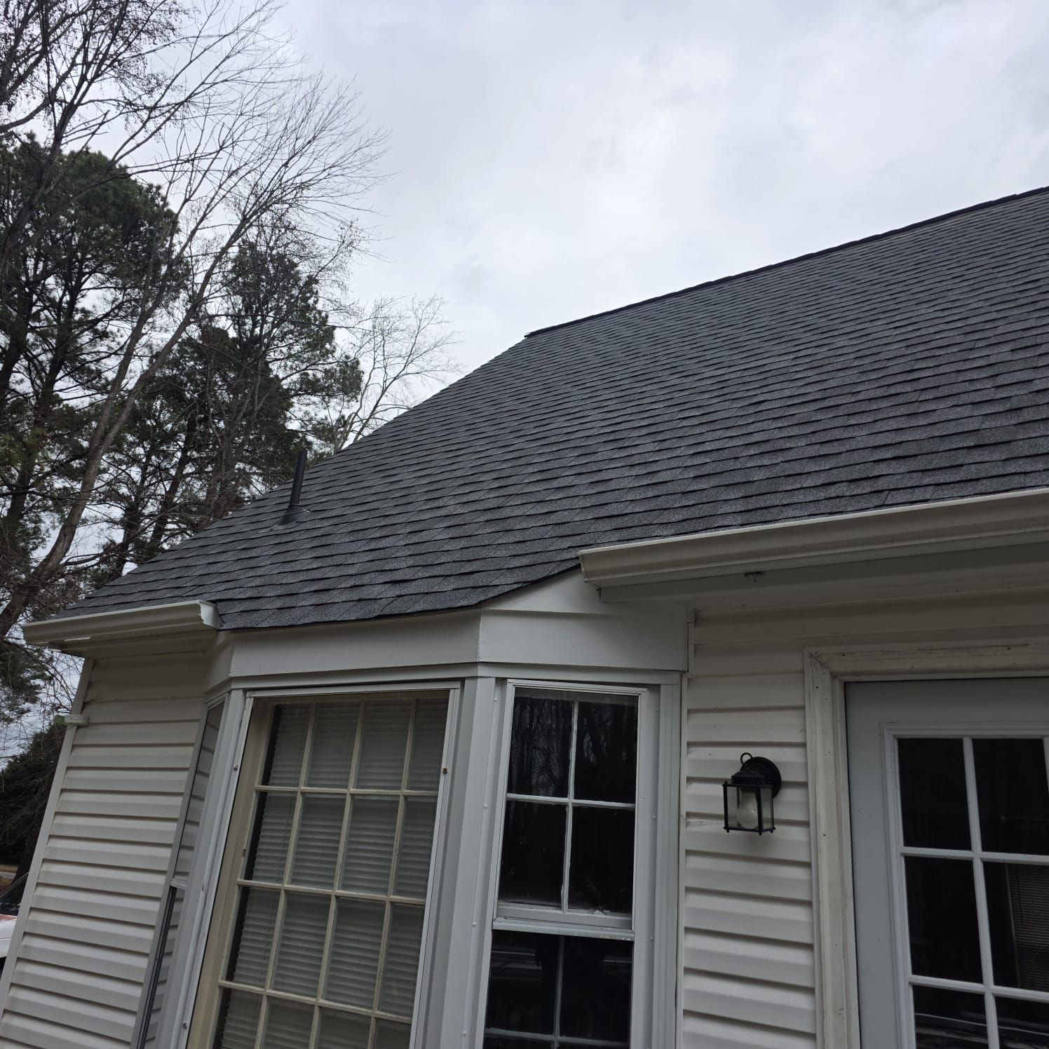 Exterior of a house with a gray shingle roof, white siding, and a cloudy sky.