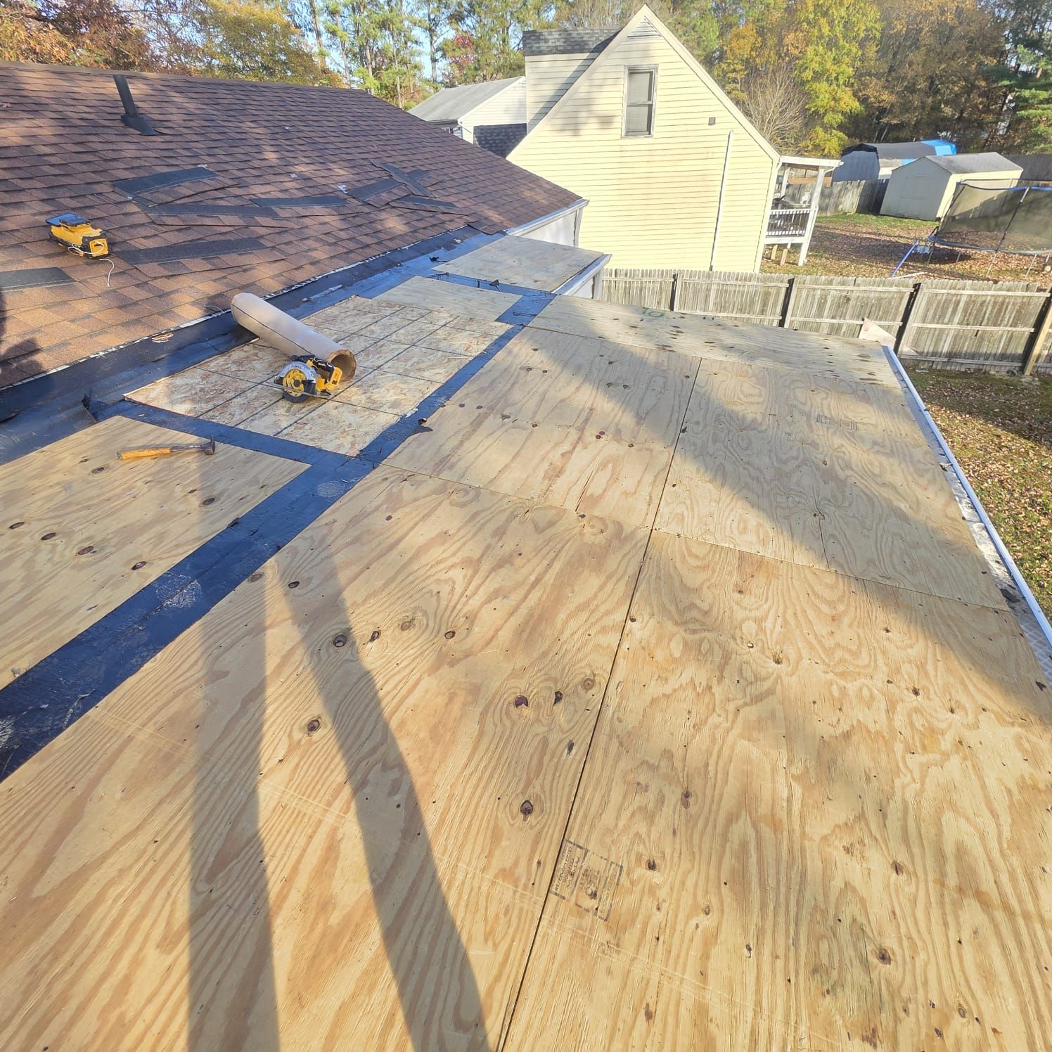 Roof with exposed plywood, black flashing, and a section with shingles. Tools are present.