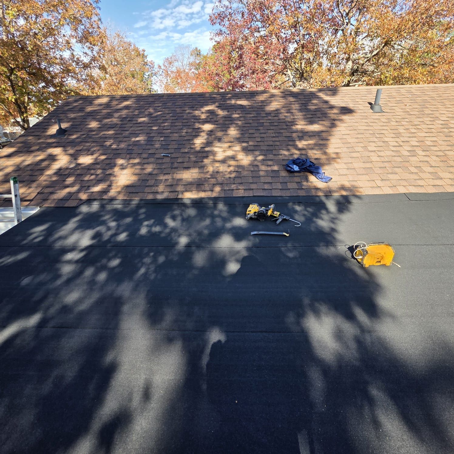 Roofers working on a house roof. One side is black, the other is brown shingles. Tools on the black section.