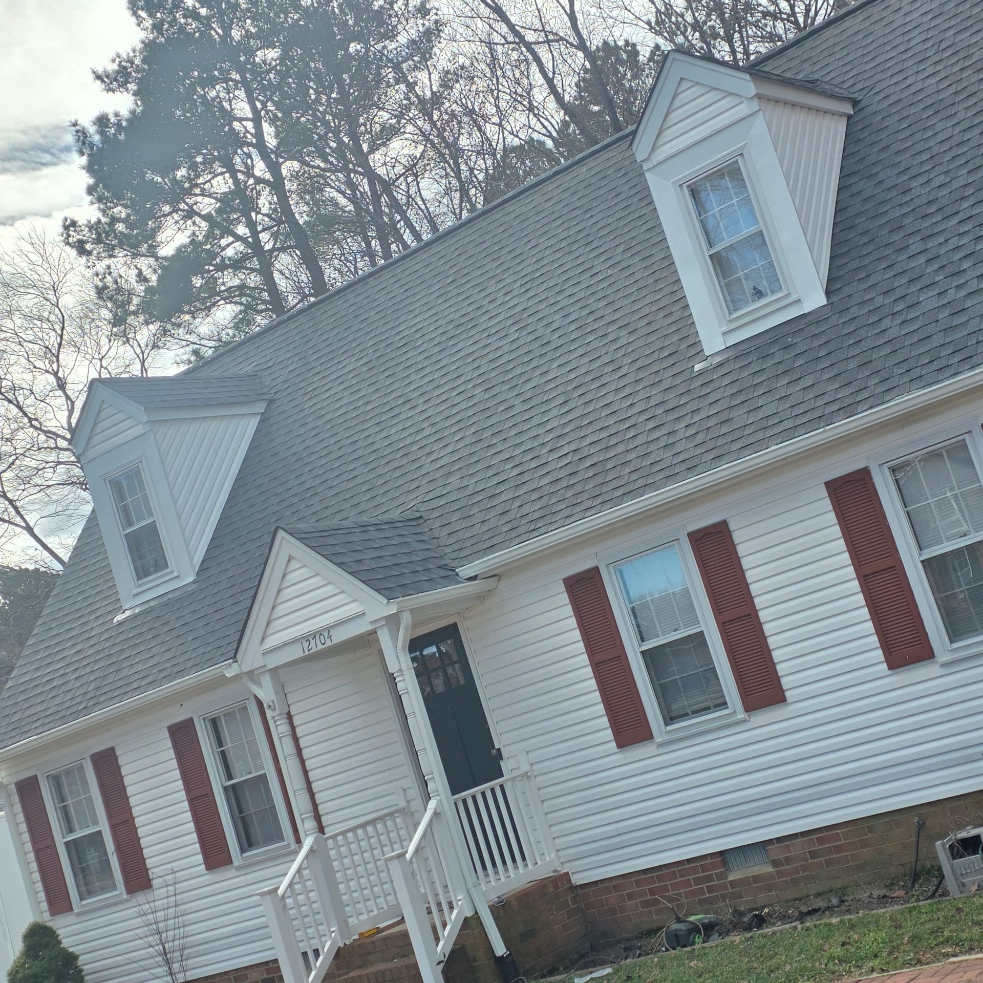 White house with gray roof, red shutters, and three dormer windows.