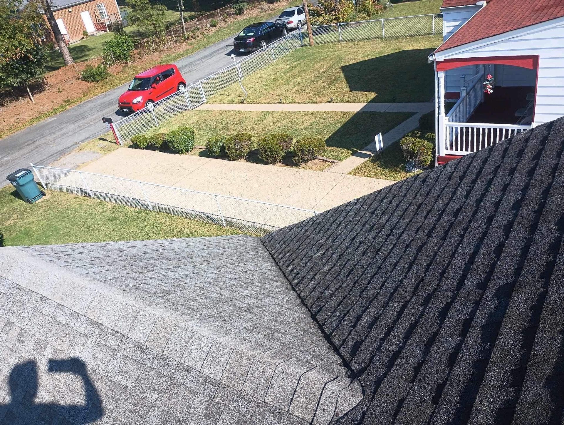 Overhead view of a street, driveway, and rooftops; a red car, green grass, and houses are visible.