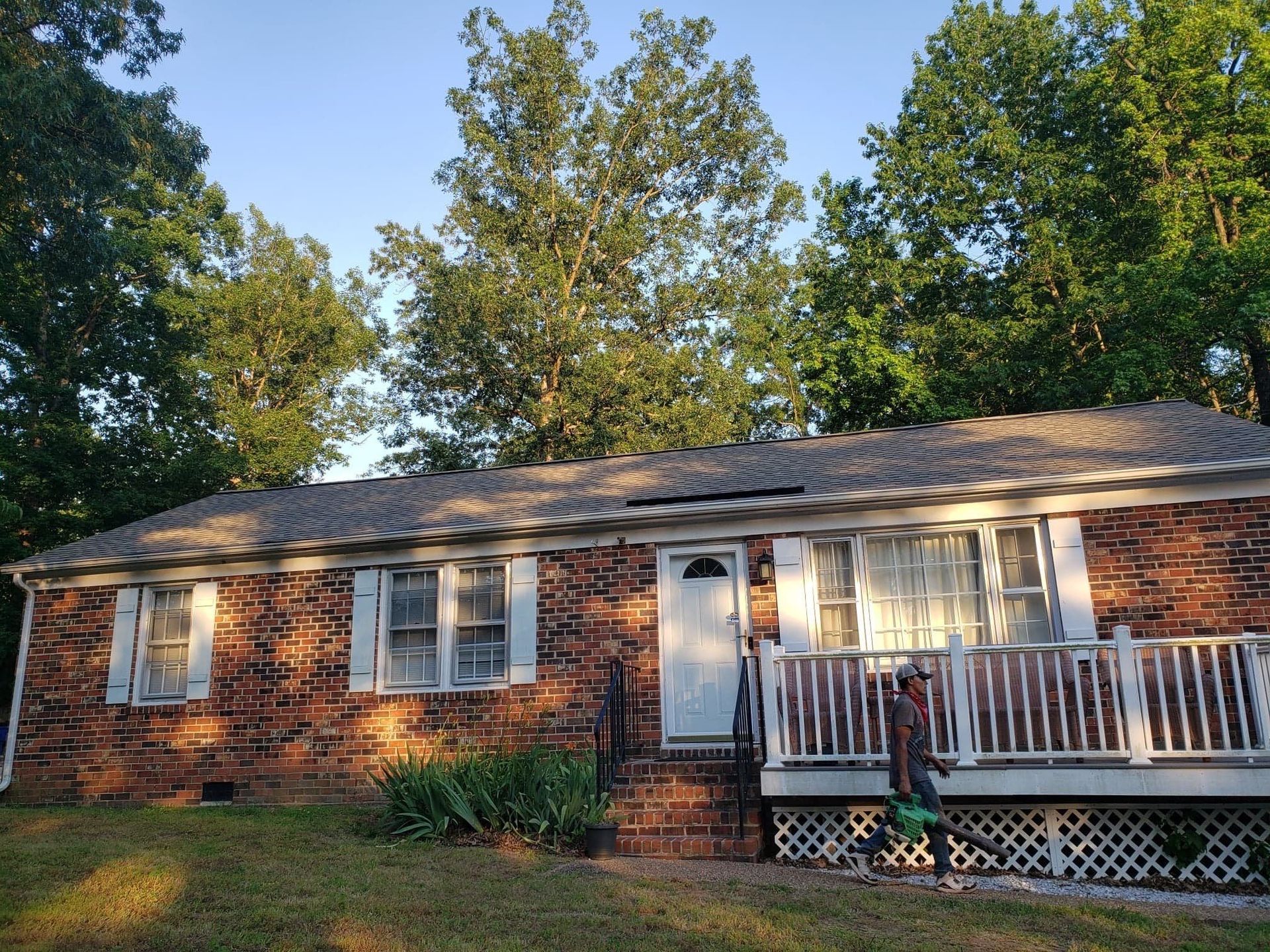 Brick house with a small porch, flanked by trees and greenery under a blue sky.