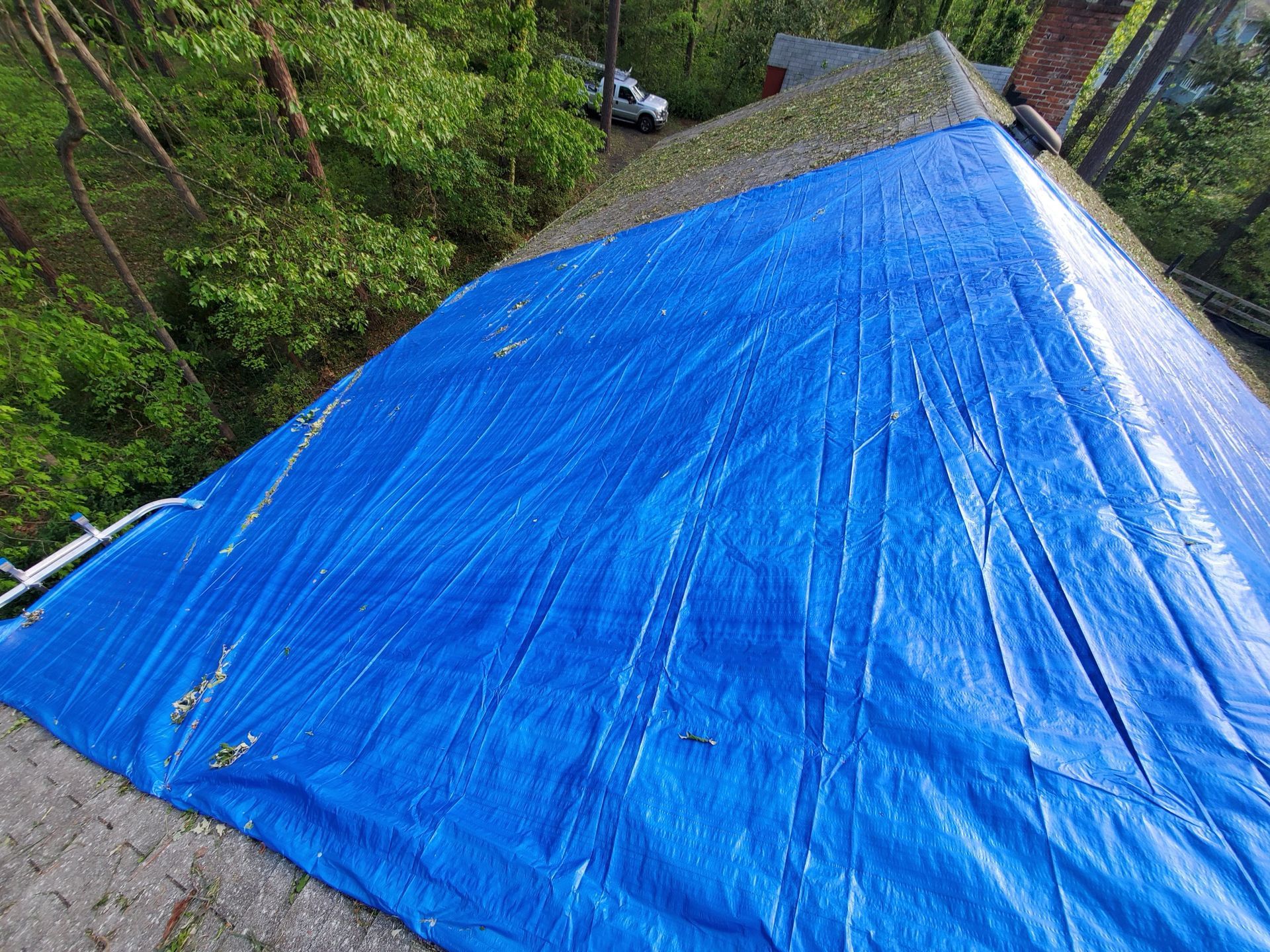 Blue tarp covering a weathered roof, with trees in the background.