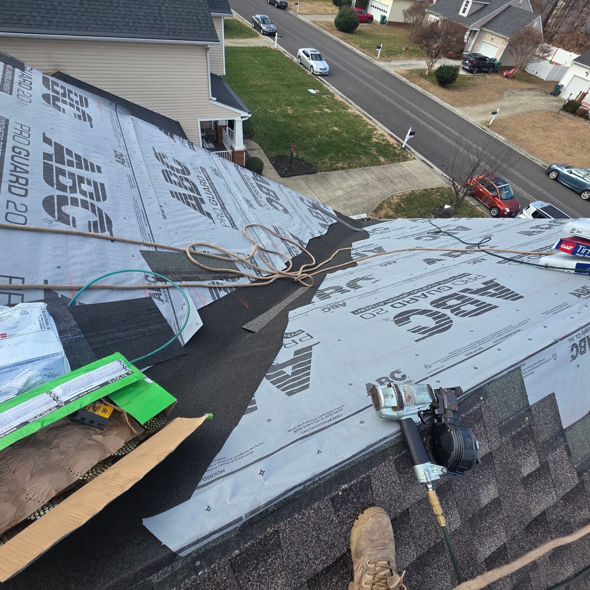 Roofer installing shingles on a house roof. Tar paper, tools, and a view of the street.