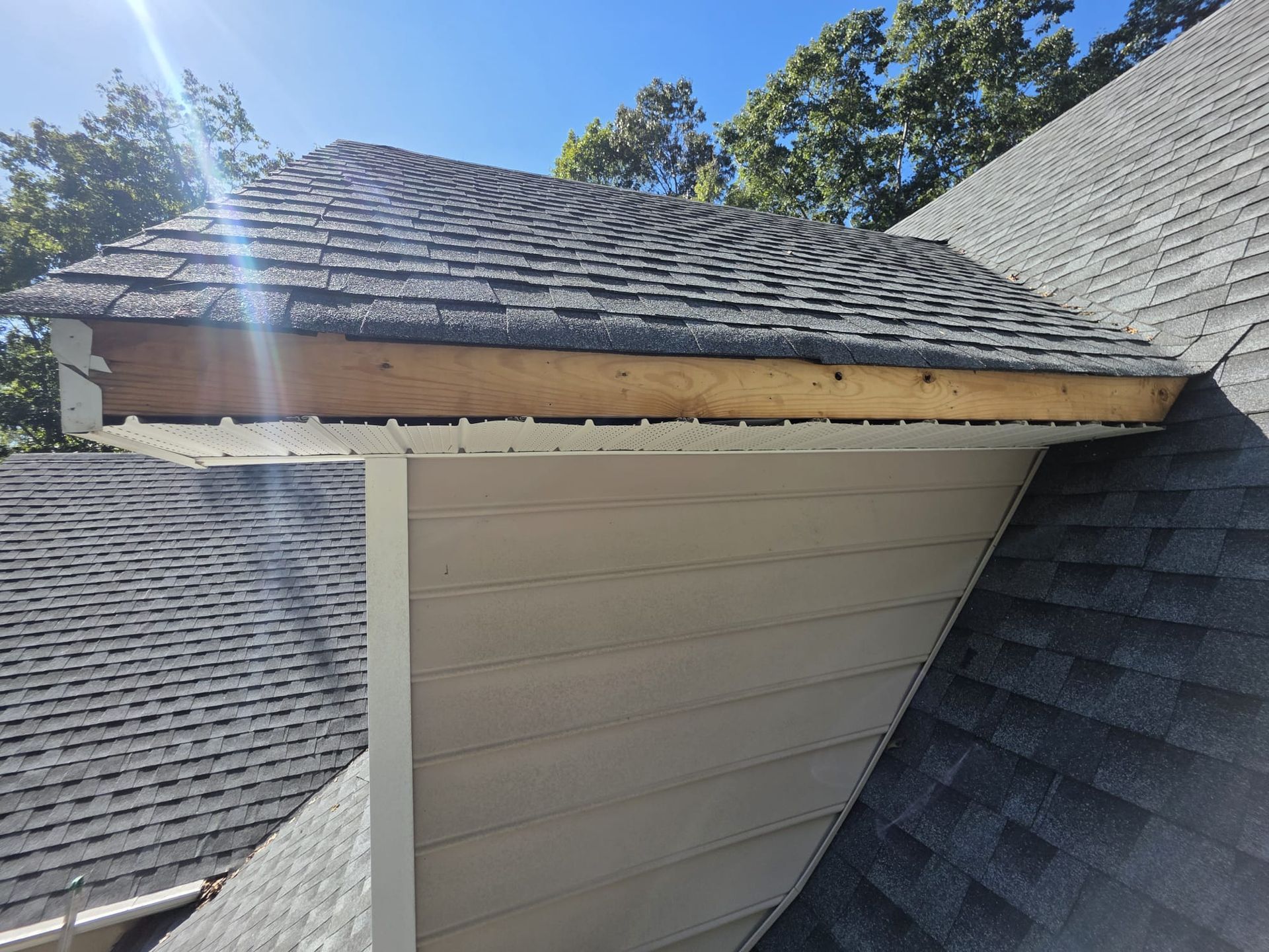 Partially constructed roof section with exposed wood and gray shingles. Beige siding below.