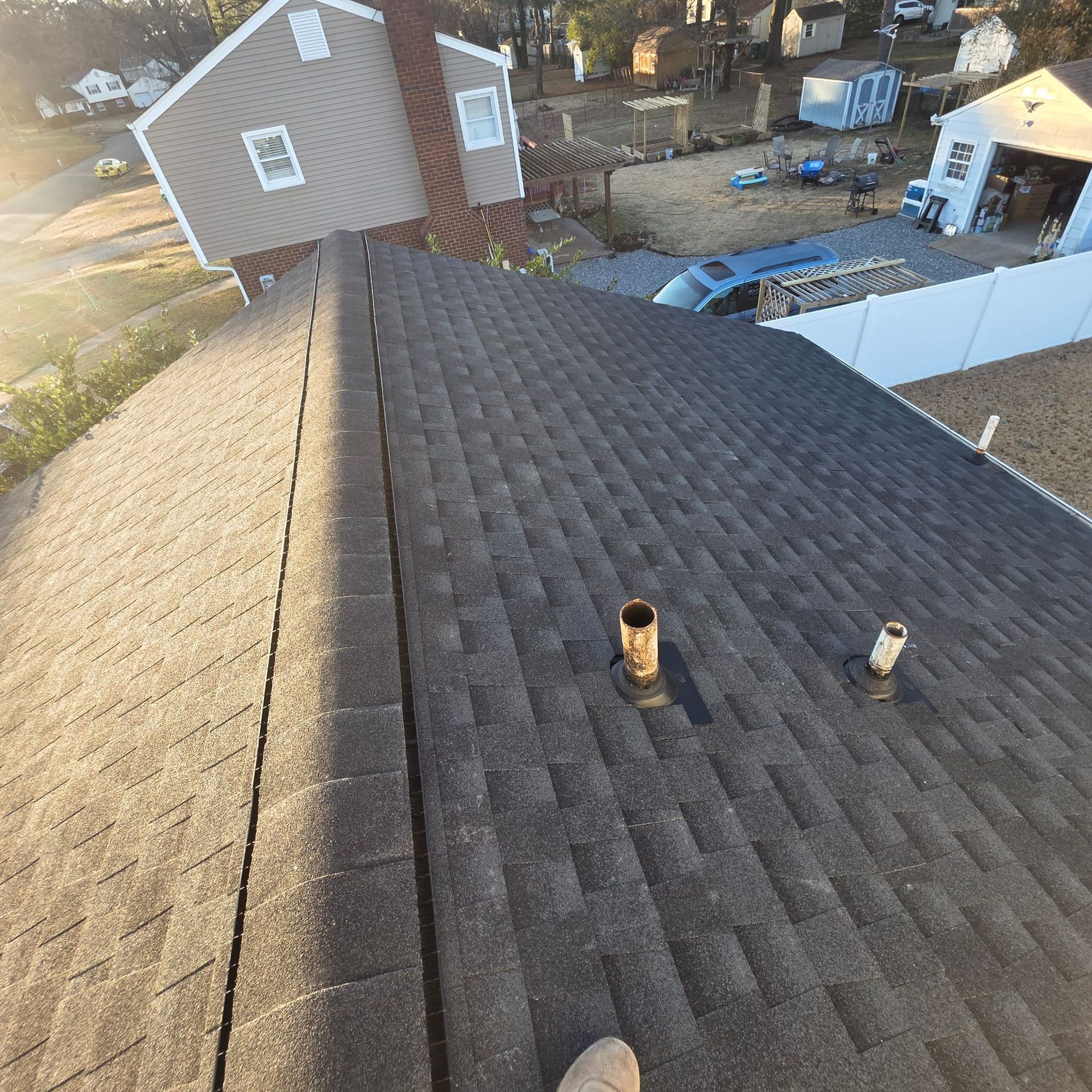 View of a dark shingle roof with two vents and a chimney against a suburban background.