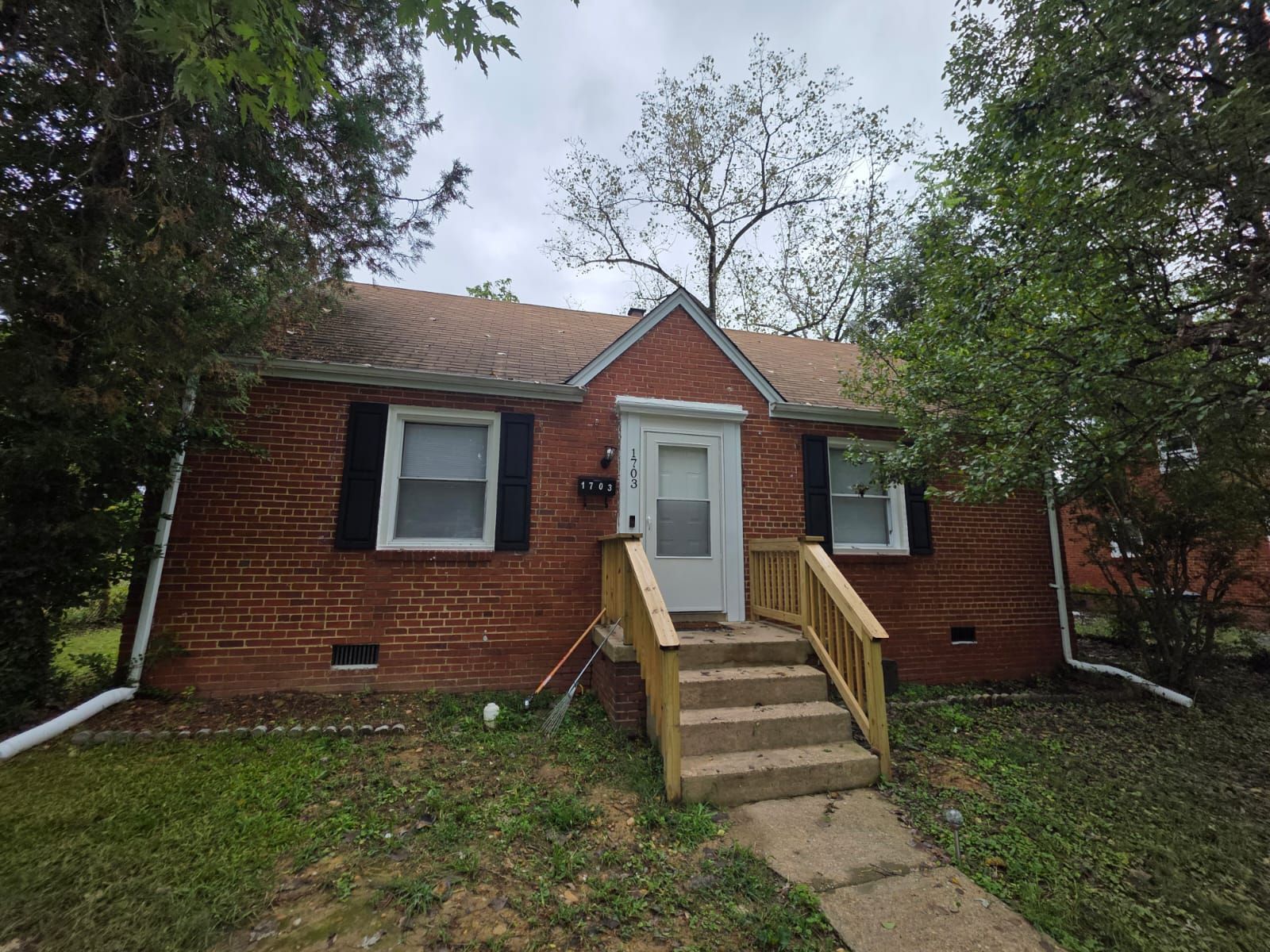 Red brick bungalow with a white door, black shutters, and wooden steps.
