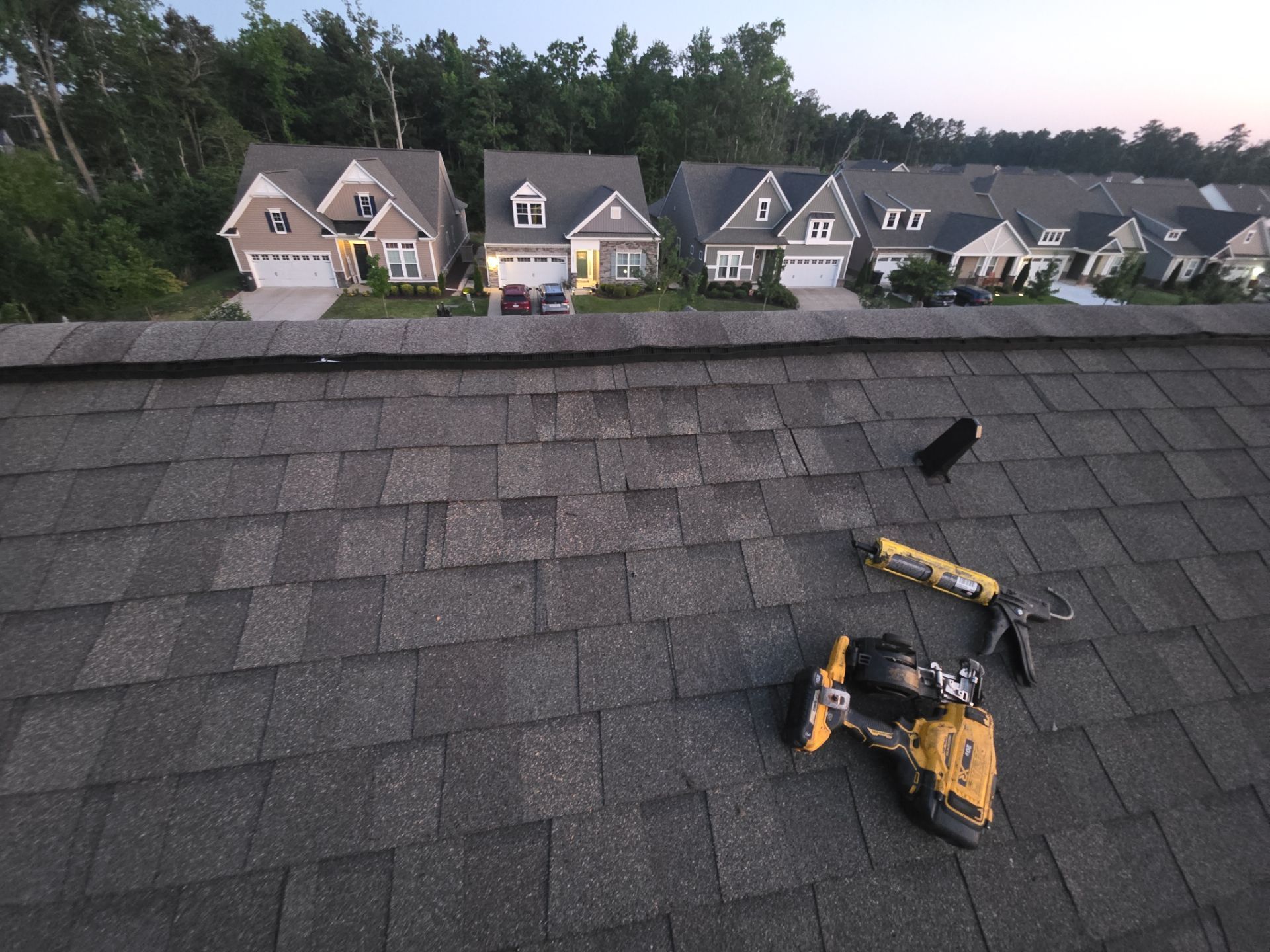 Roofing tools on a shingled roof with a suburban row of houses in the background at dusk