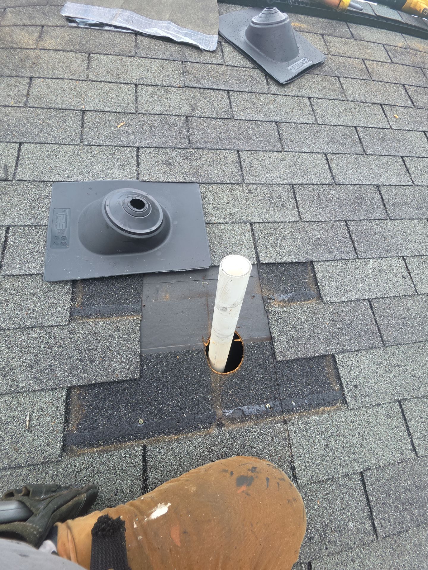 Roof shingles with two vents and a white pipe protruding through a cut opening.