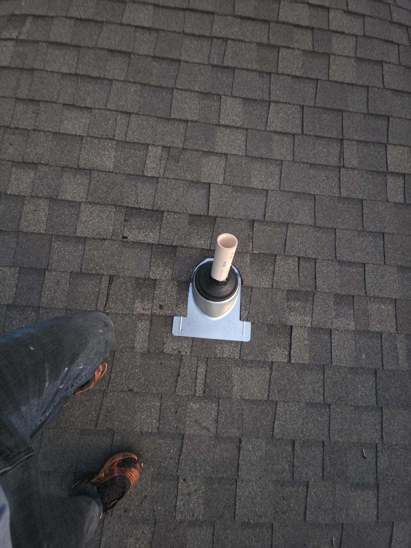 Roof vent pipe with a white flashing on dark asphalt shingles; part of a shoe is visible at bottom left.