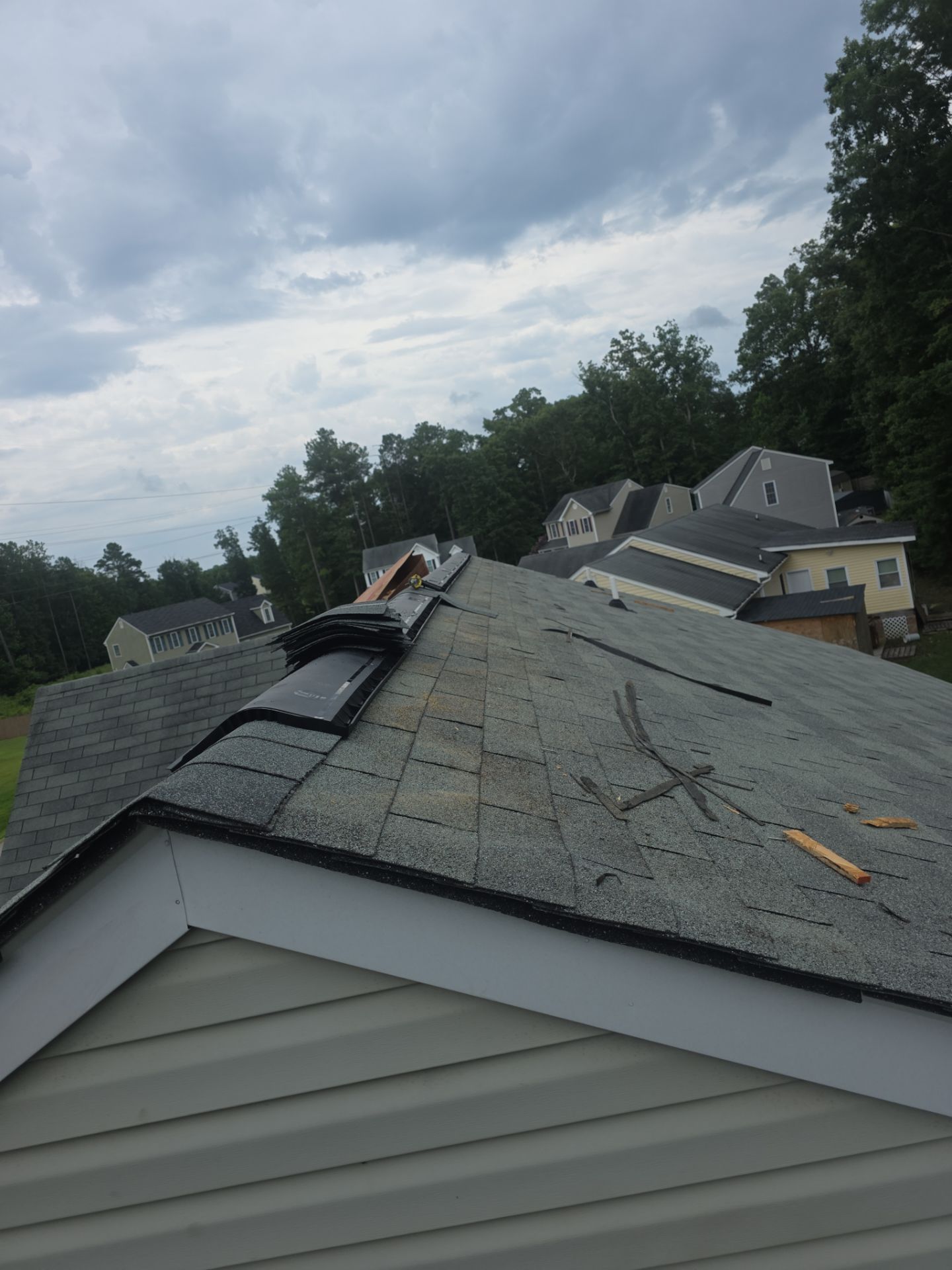 Roof damaged by fallen tree branch, with shingles torn and a cloudy sky overhead