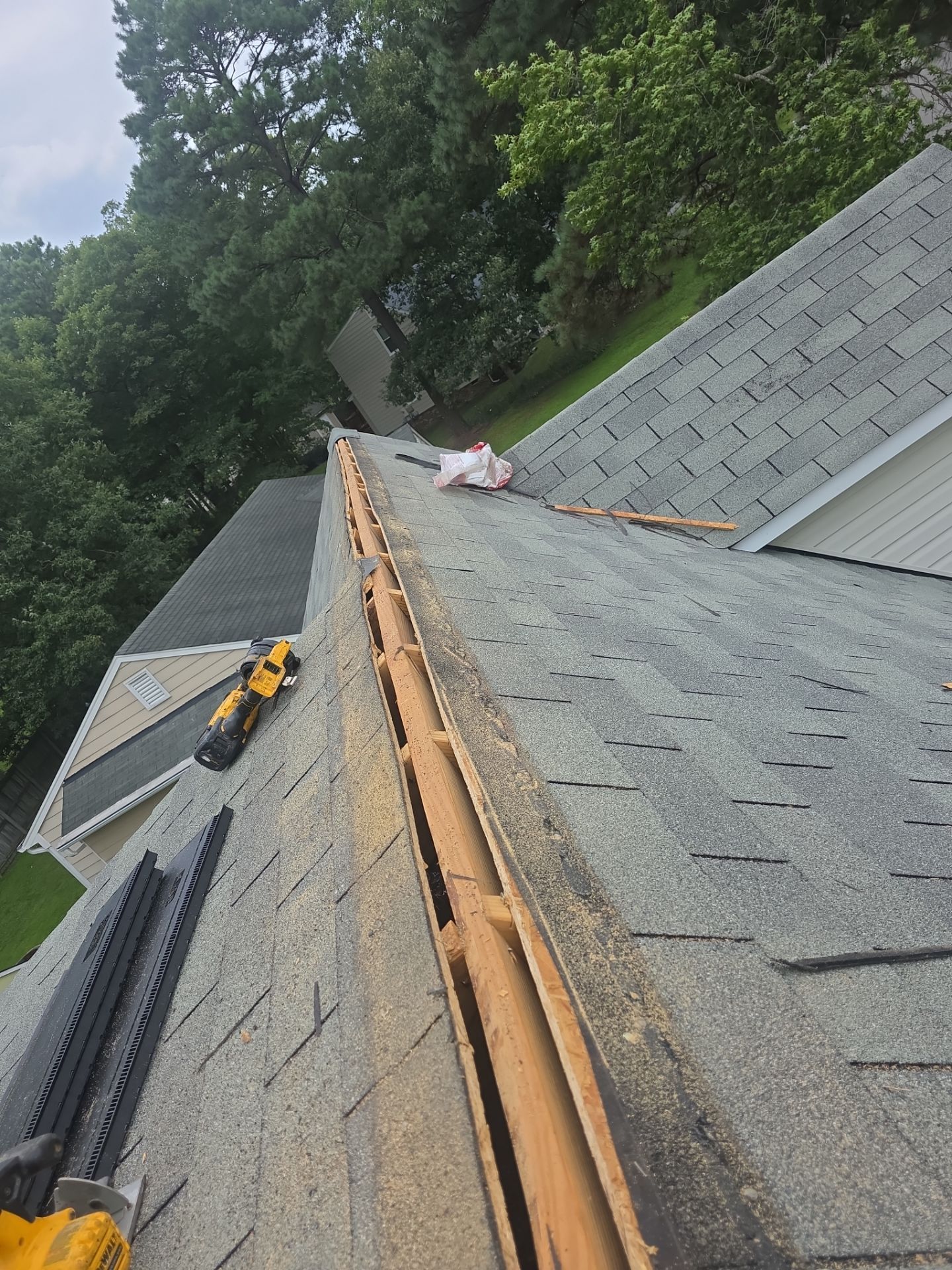 Roof repair materials and tools on a shingled roof with a person working near the ridge line.