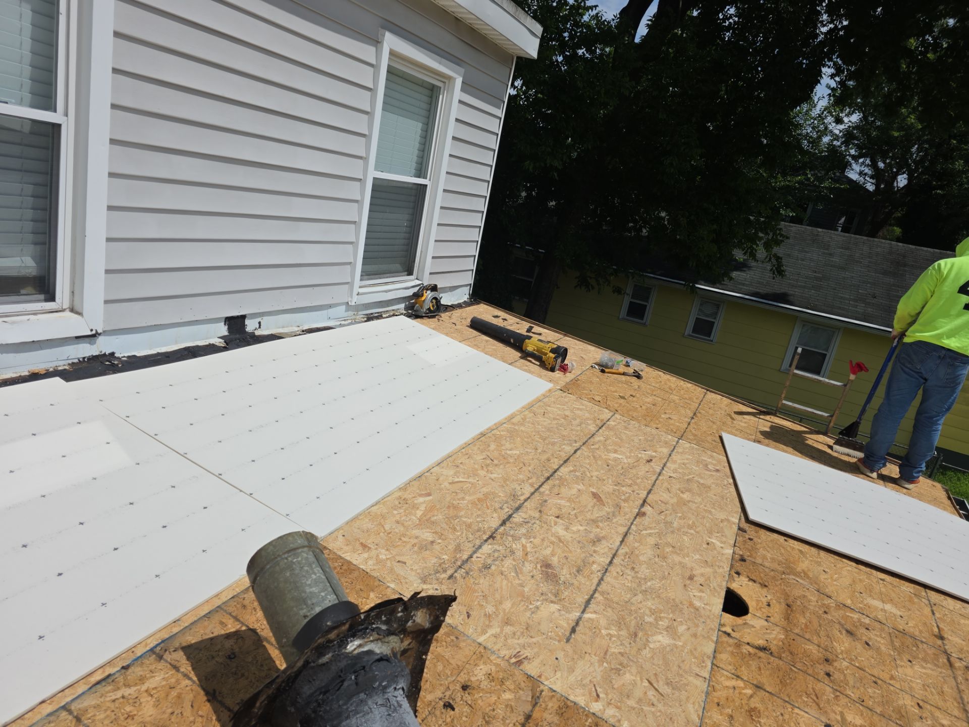 Roofing underlayment being installed on a house roof, with a worker at the right edge.