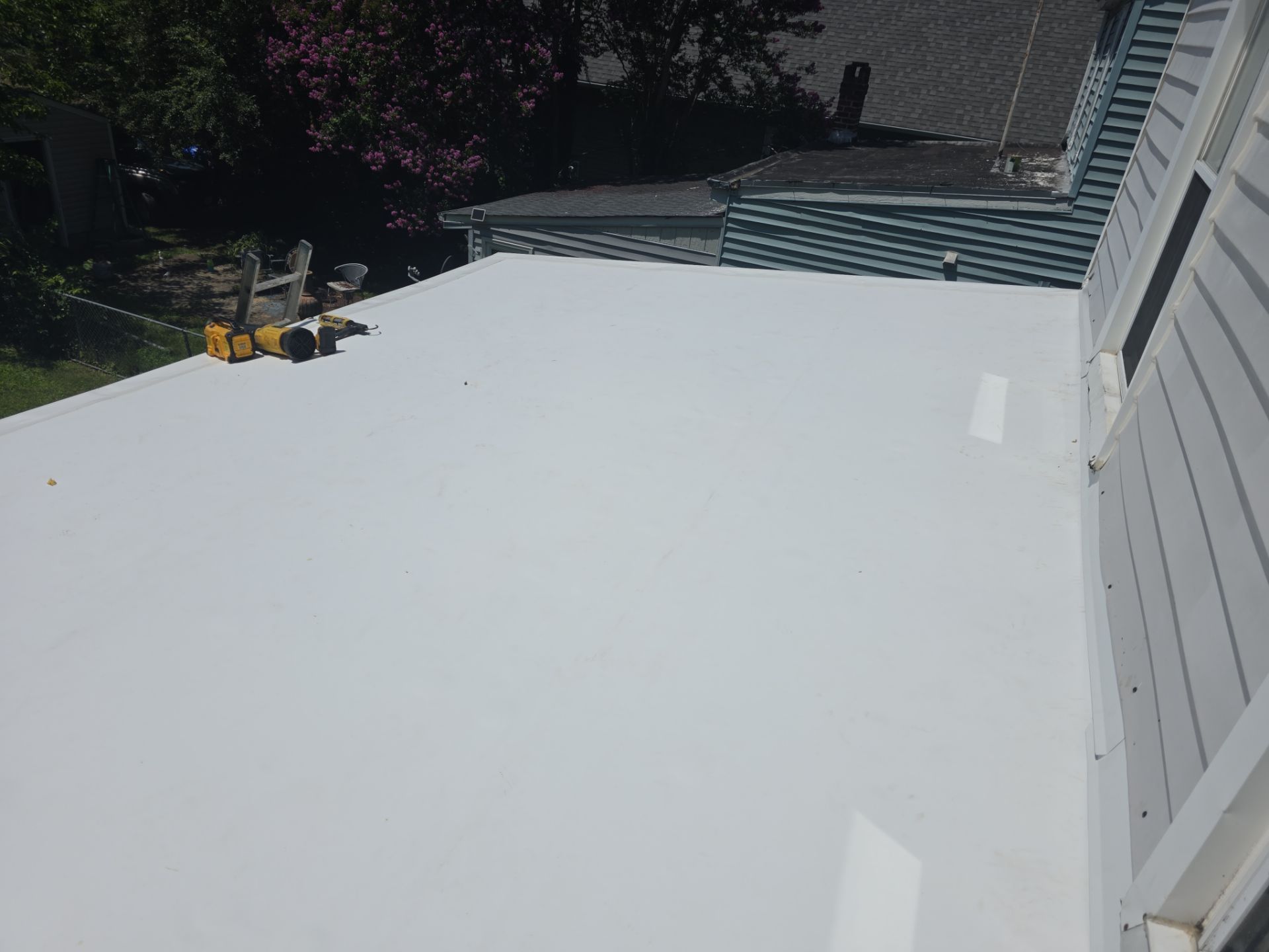 Freshly coated white roof deck beside a house, with a small yellow tool near the back steps.