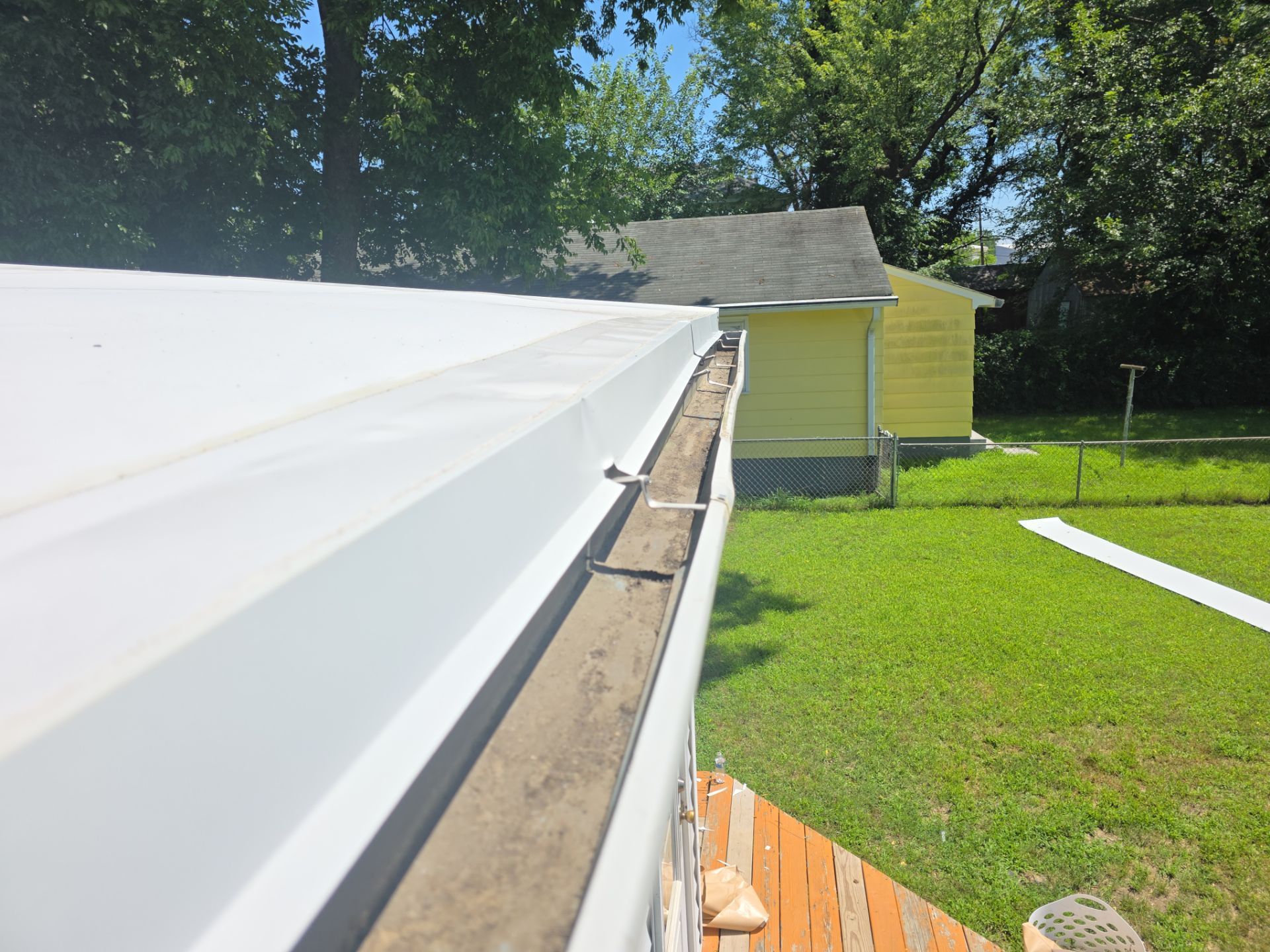 Close-up of white roofing material being installed on a wooden roof edge beside a yellow shed.