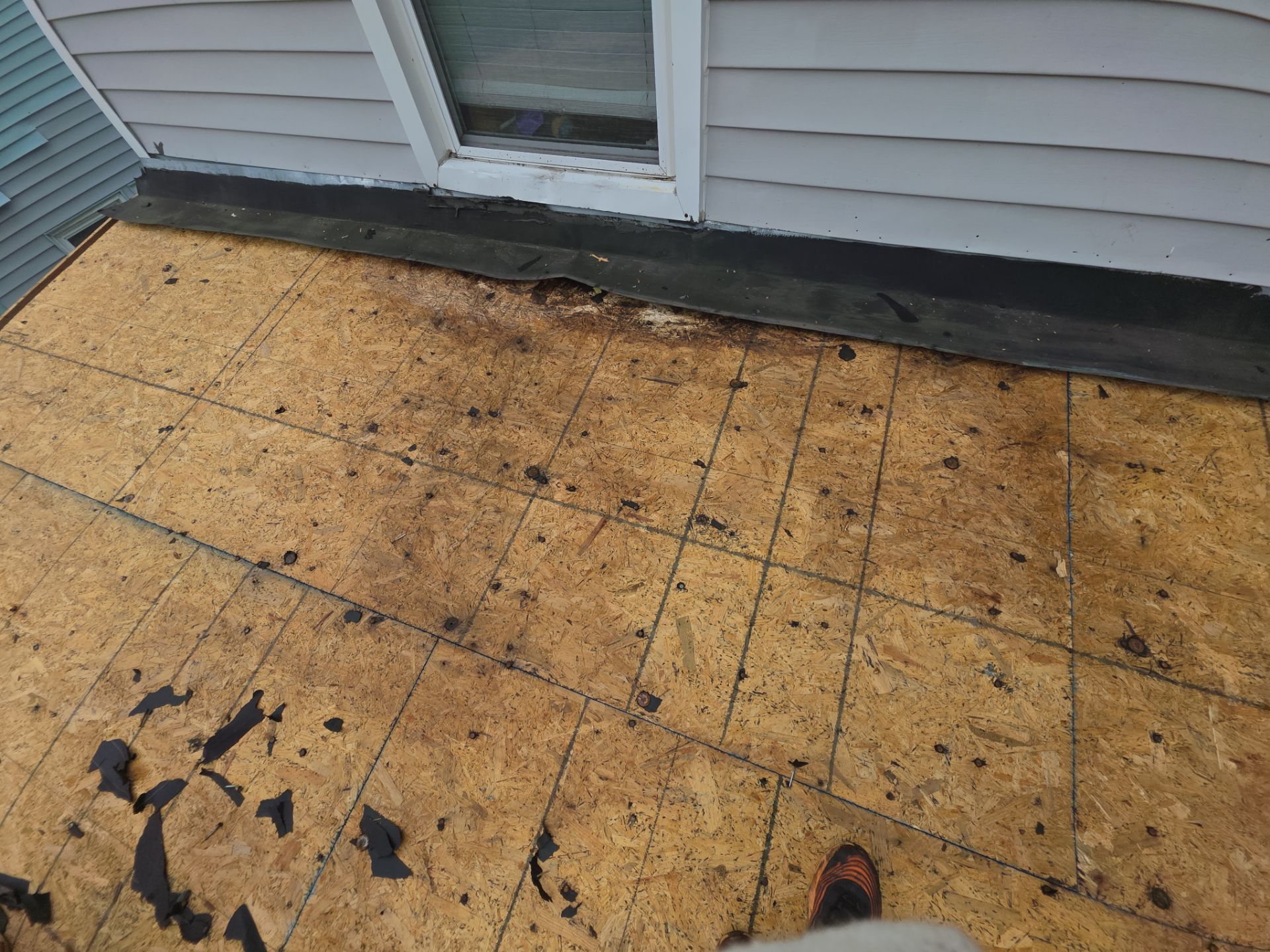 Partial roof deck with exposed OSB sheathing beside gray house siding and a window