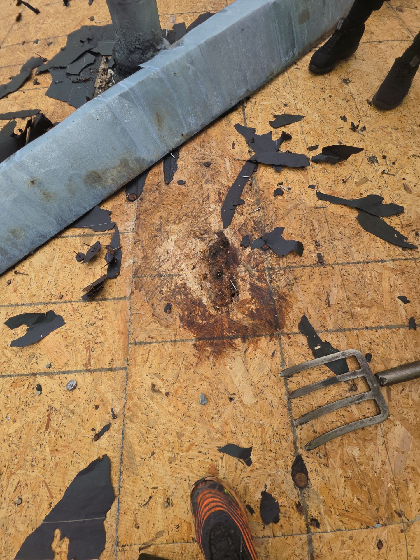 Dirty rooftop with scattered black debris, a stained wooden surface, and a blue metal beam.