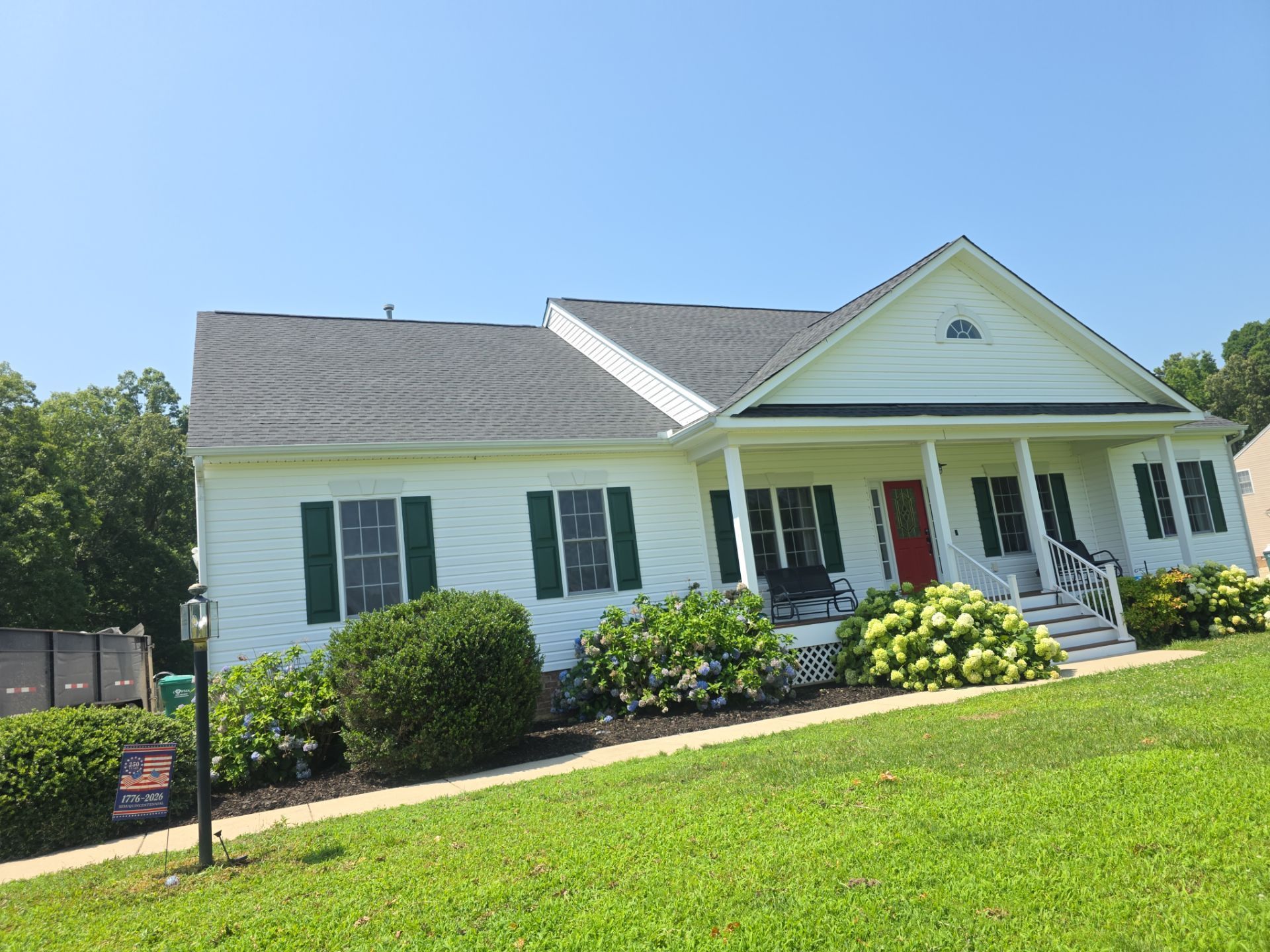 White house with green shutters, front porch, and manicured lawn under a clear blue sky