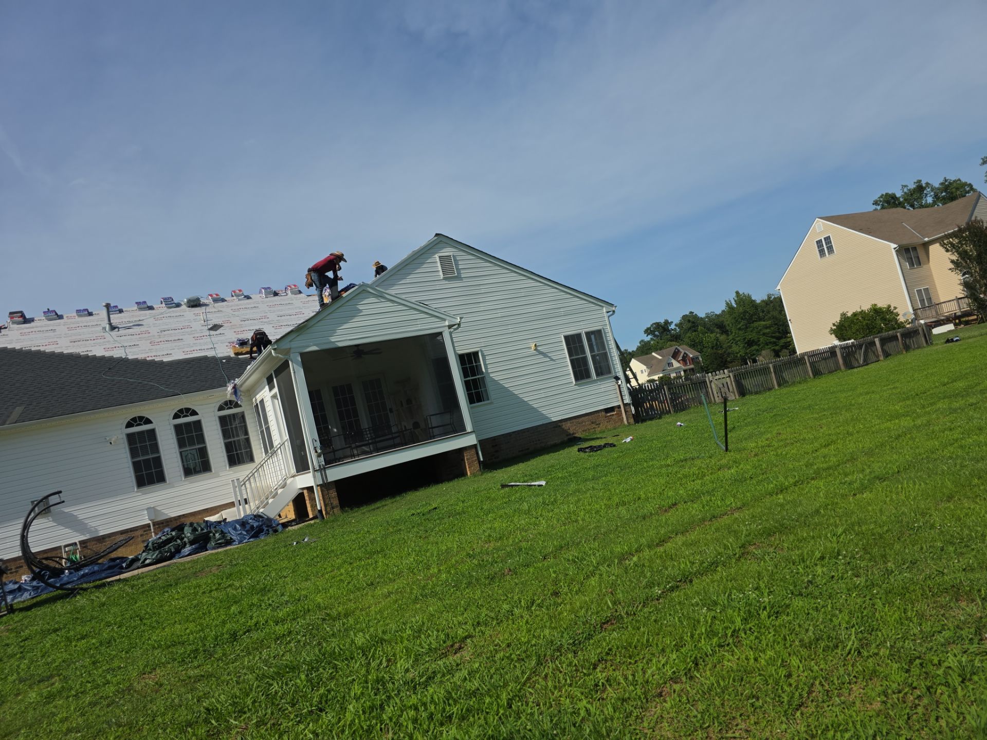 Tilted view of a green lawn with a pale blue house and neighboring homes under a clear sky