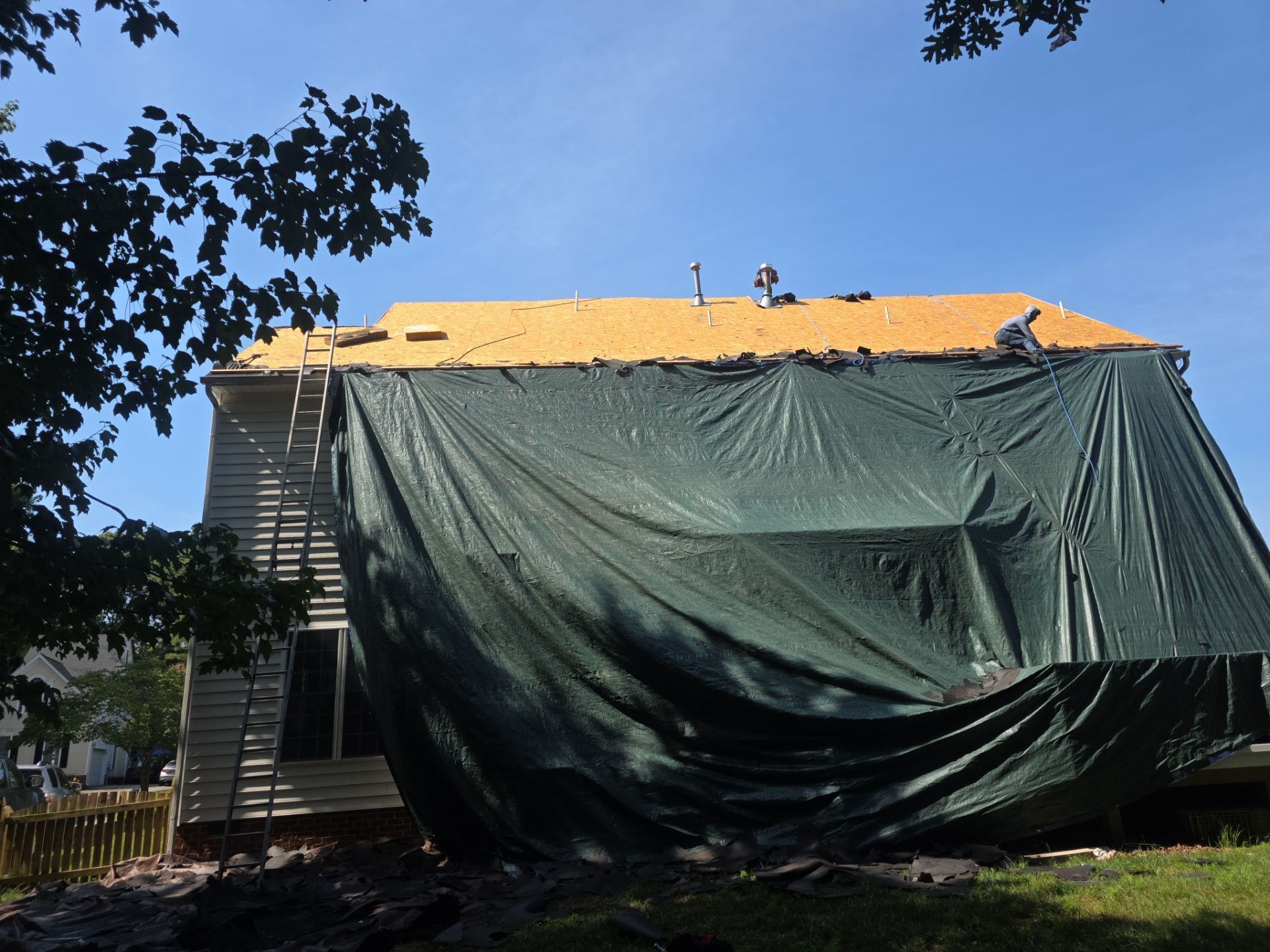 House under repair covered with green tarp and orange roof under a blue sky