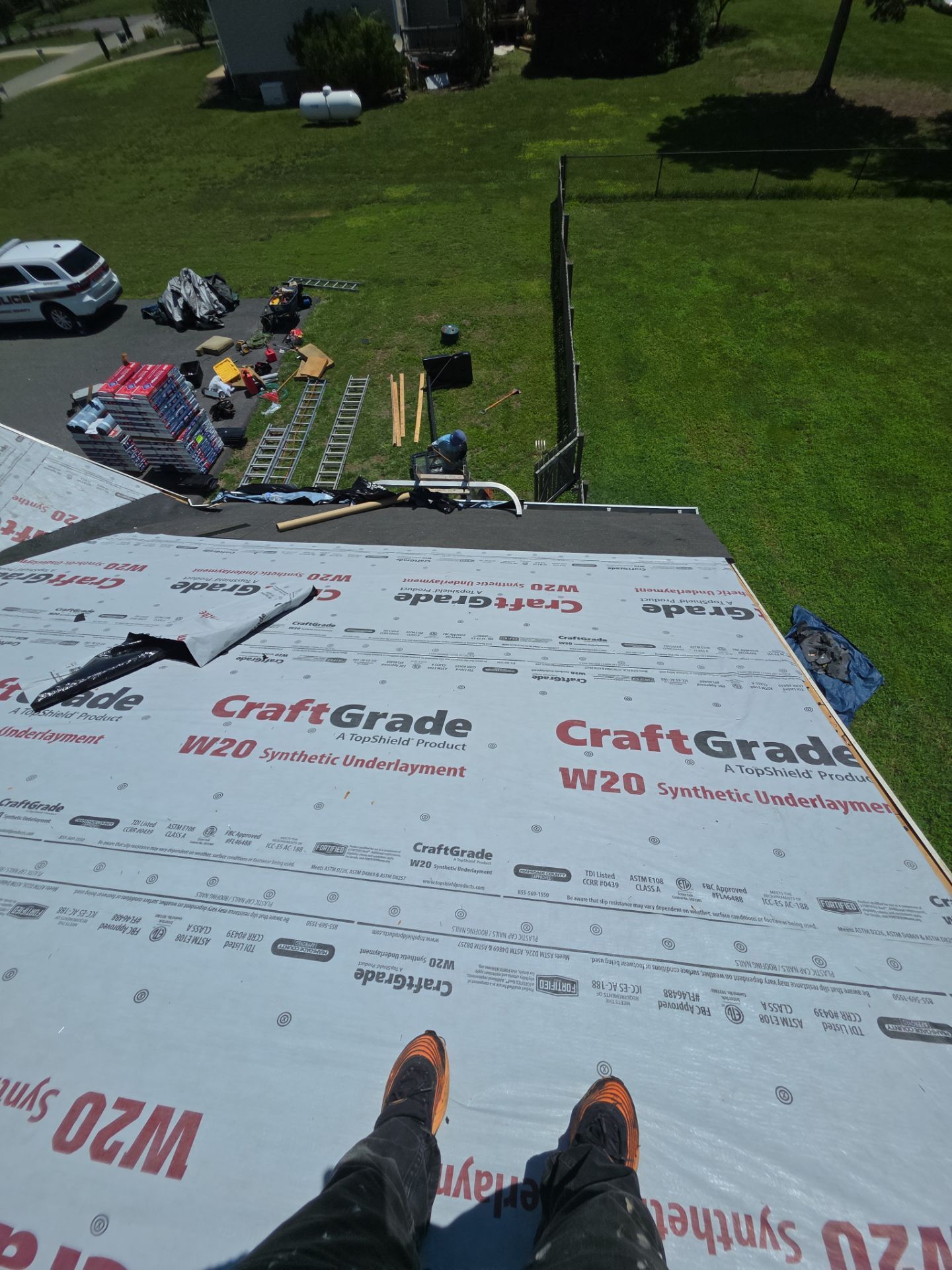 Roofing work in progress, with tools and materials on a shingled roof overlooking a grassy yard