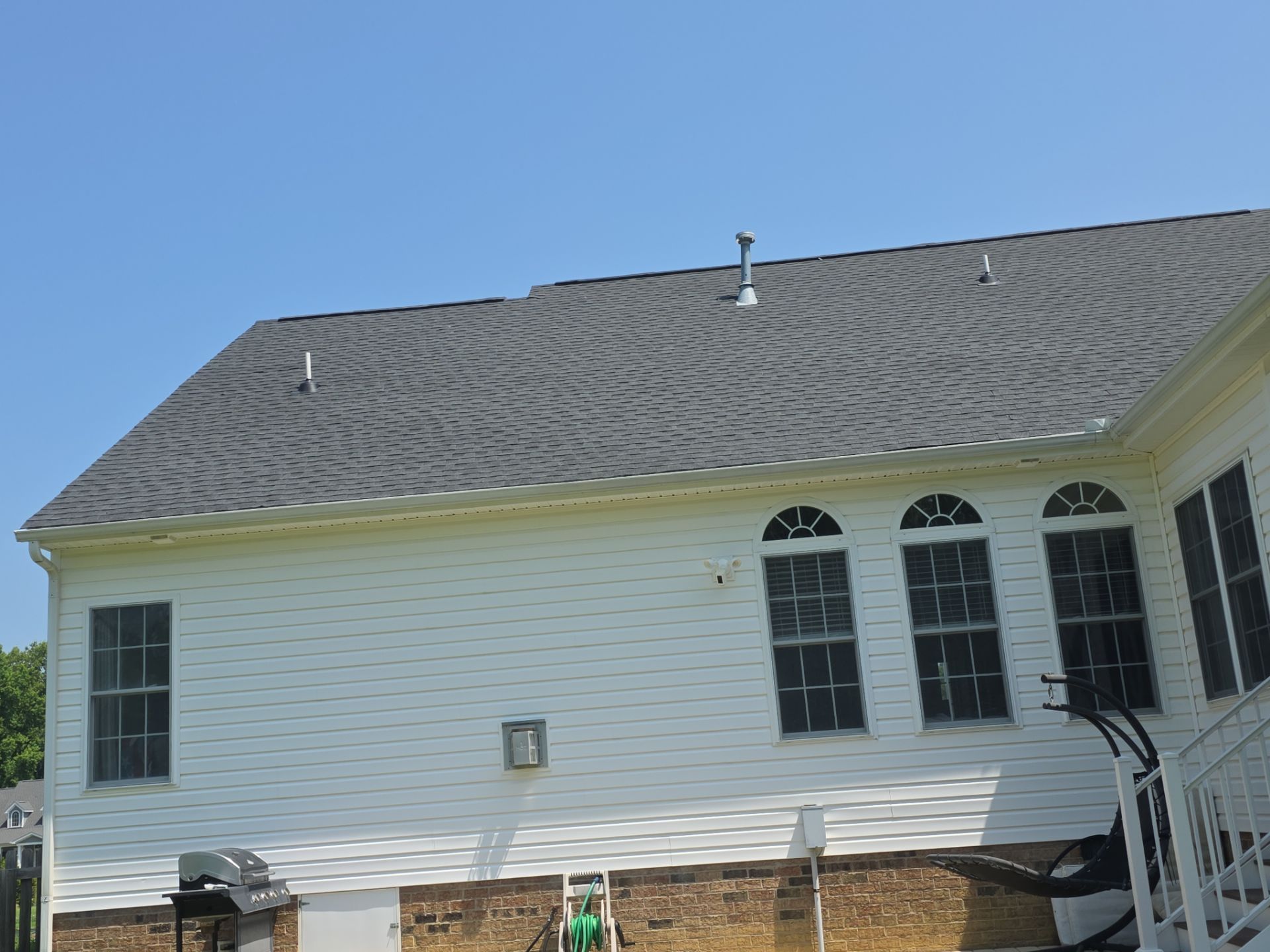 White house exterior with gray shingled roof, windows, and front steps under a clear blue sky