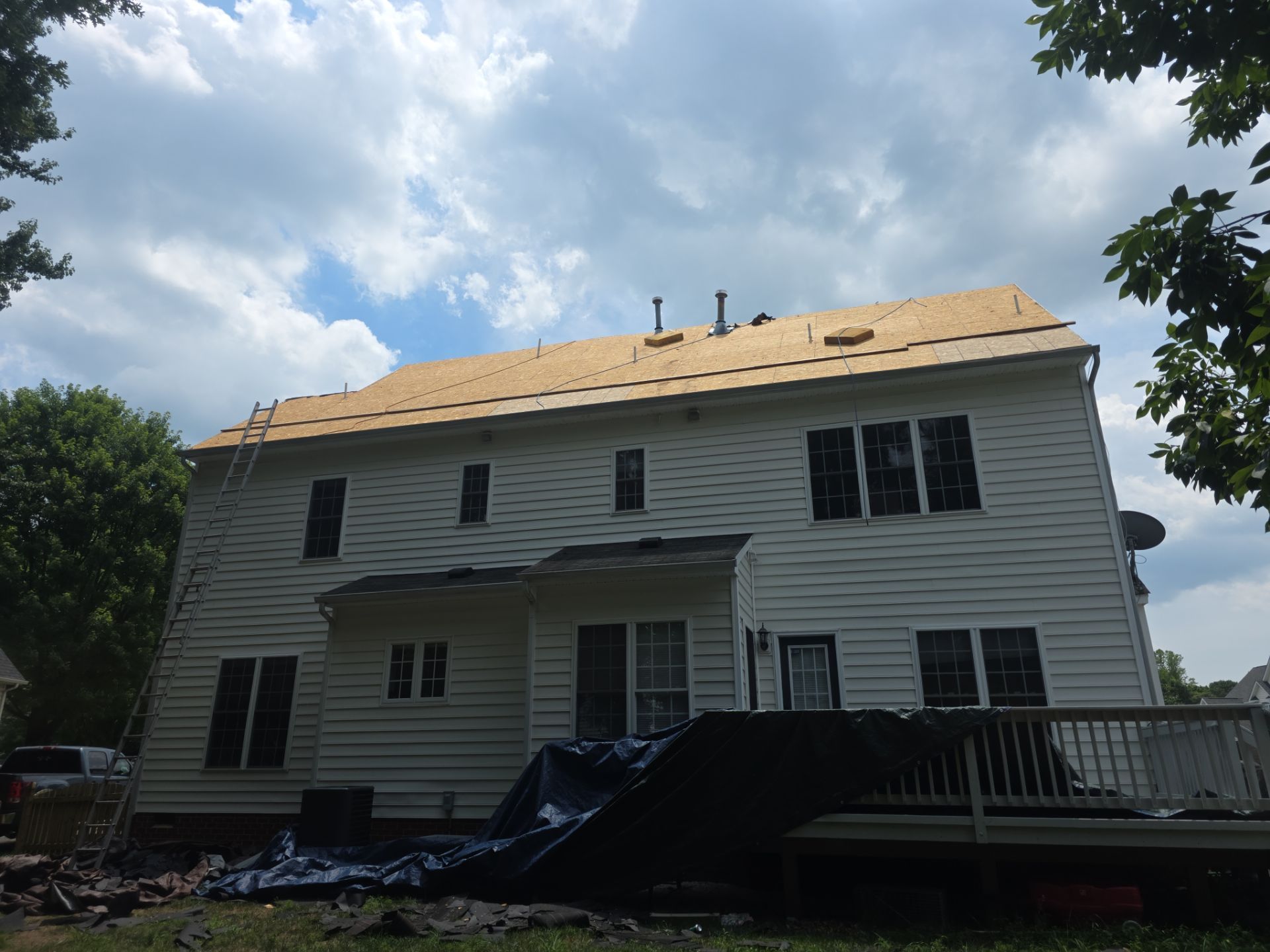 Damaged two-story house with exposed roof under repair, surrounded by debris and a cloudy sky