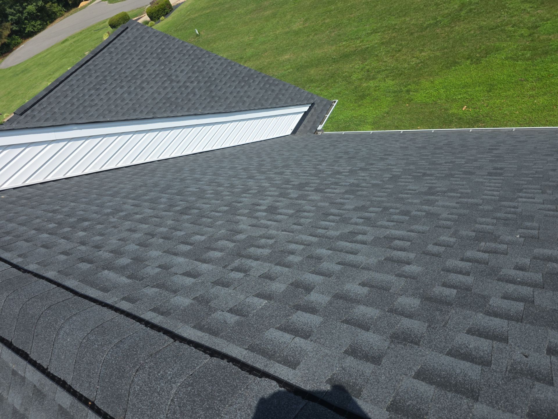 Dark gray shingled roof with a white metal section beside a grassy hillside