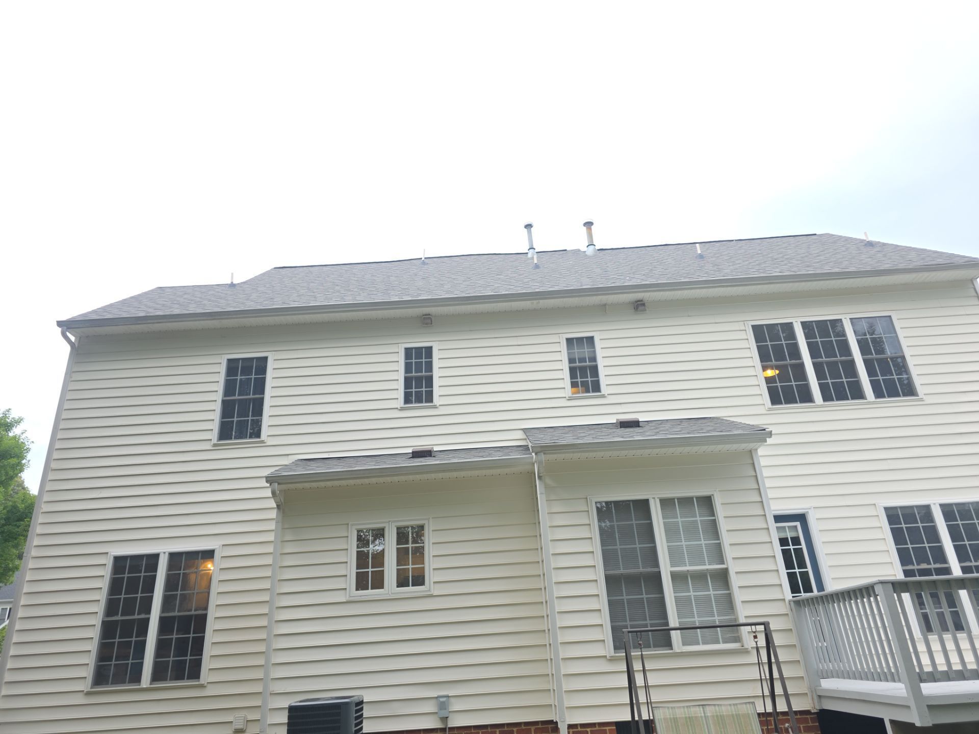 Two-story beige house with gray roof, windows, and a front porch under a bright sky