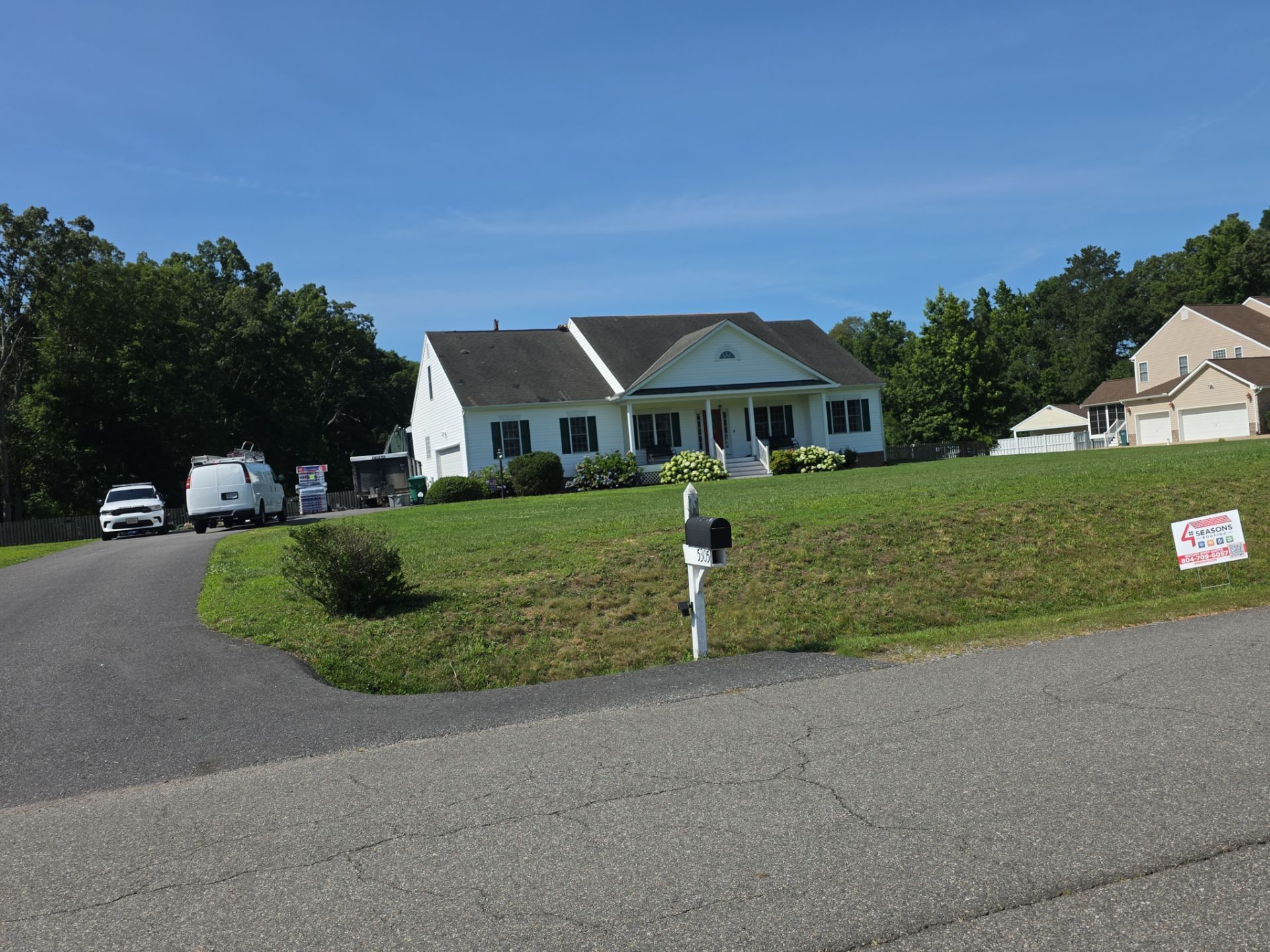 White ranch house with a driveway, lawn, parked vehicles, and a small mailbox on a sunny day