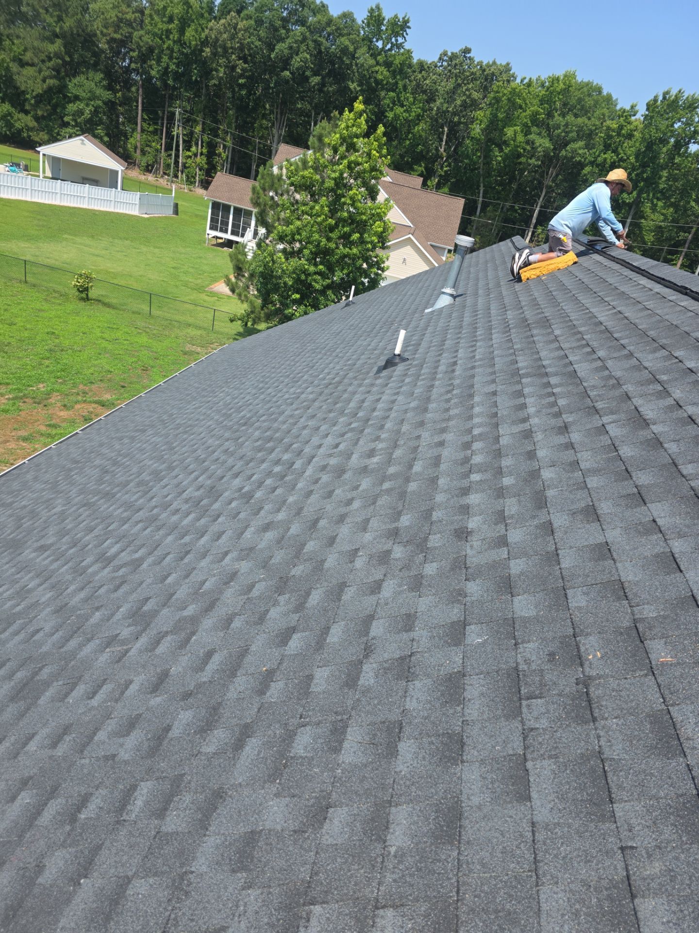 Worker on a steep shingled roof using a tool on a sunny day