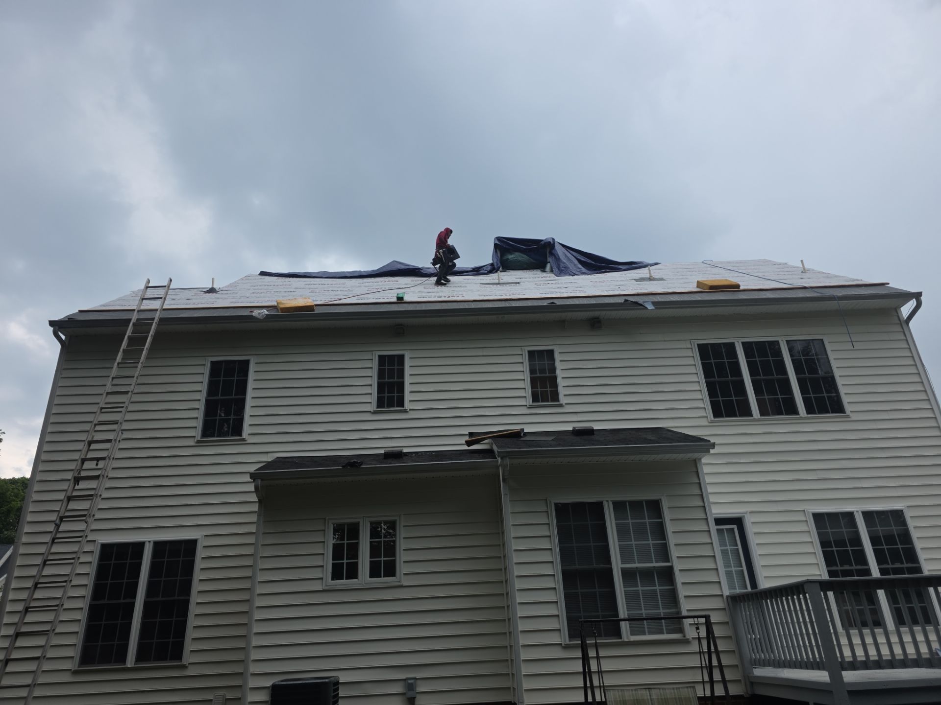 House with roof damage and workers repairing it under a cloudy sky