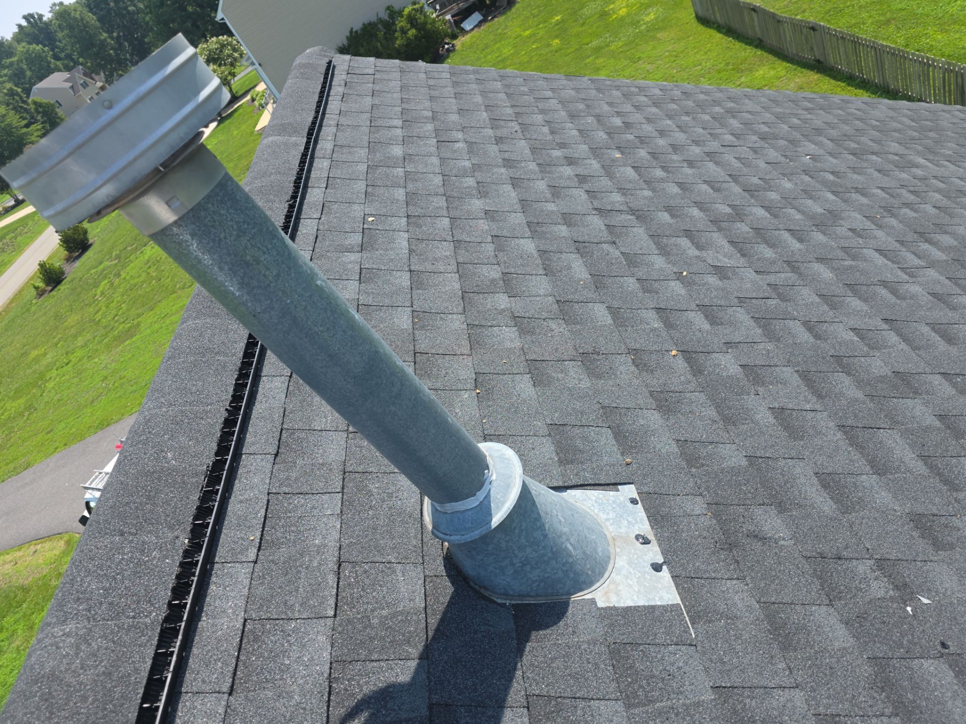 Roof vent pipe on gray shingled roof with a metal flashing base